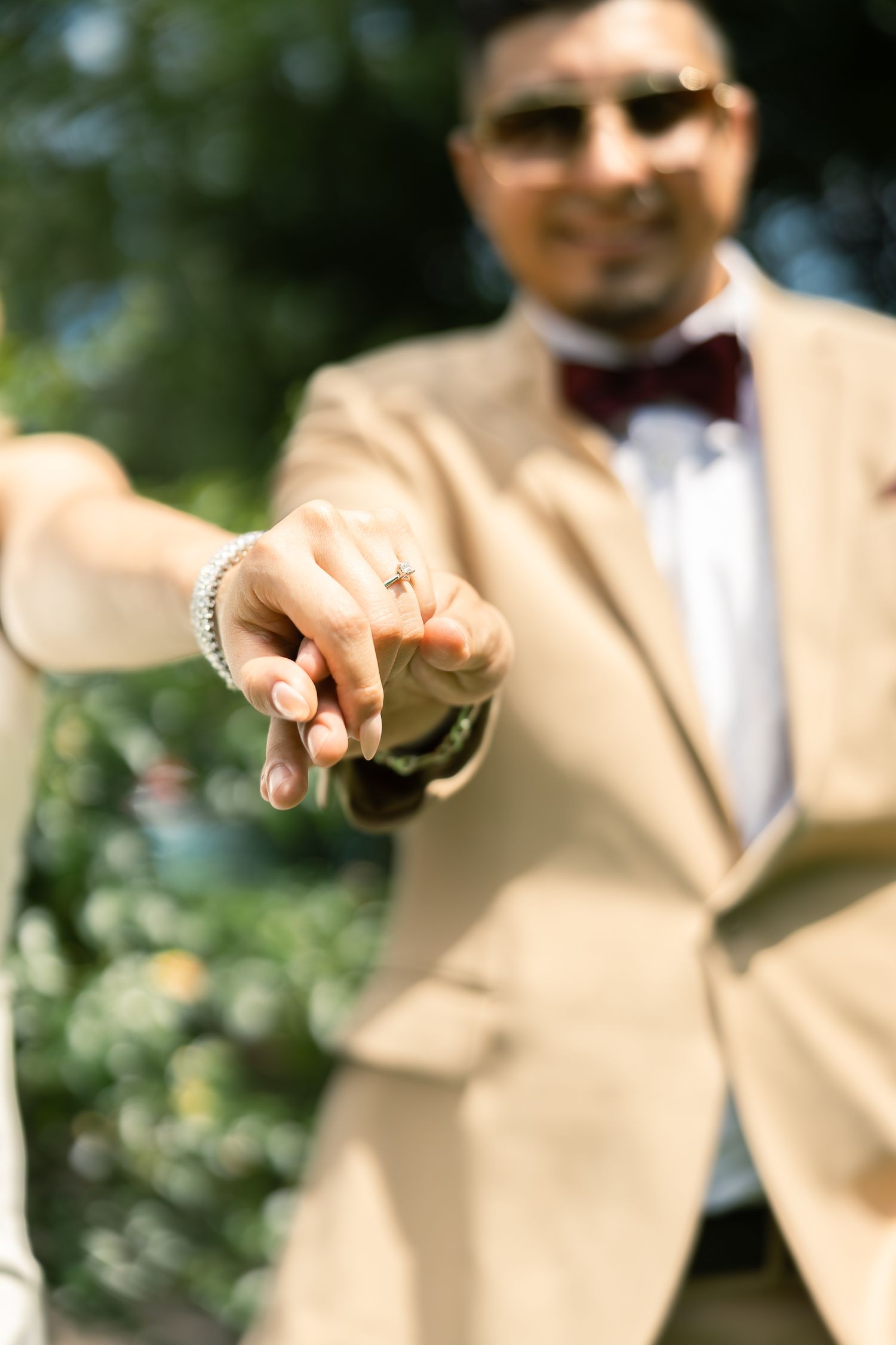 Close up shot of groom in beige suit and bowtie showing wedding ring against garden background.