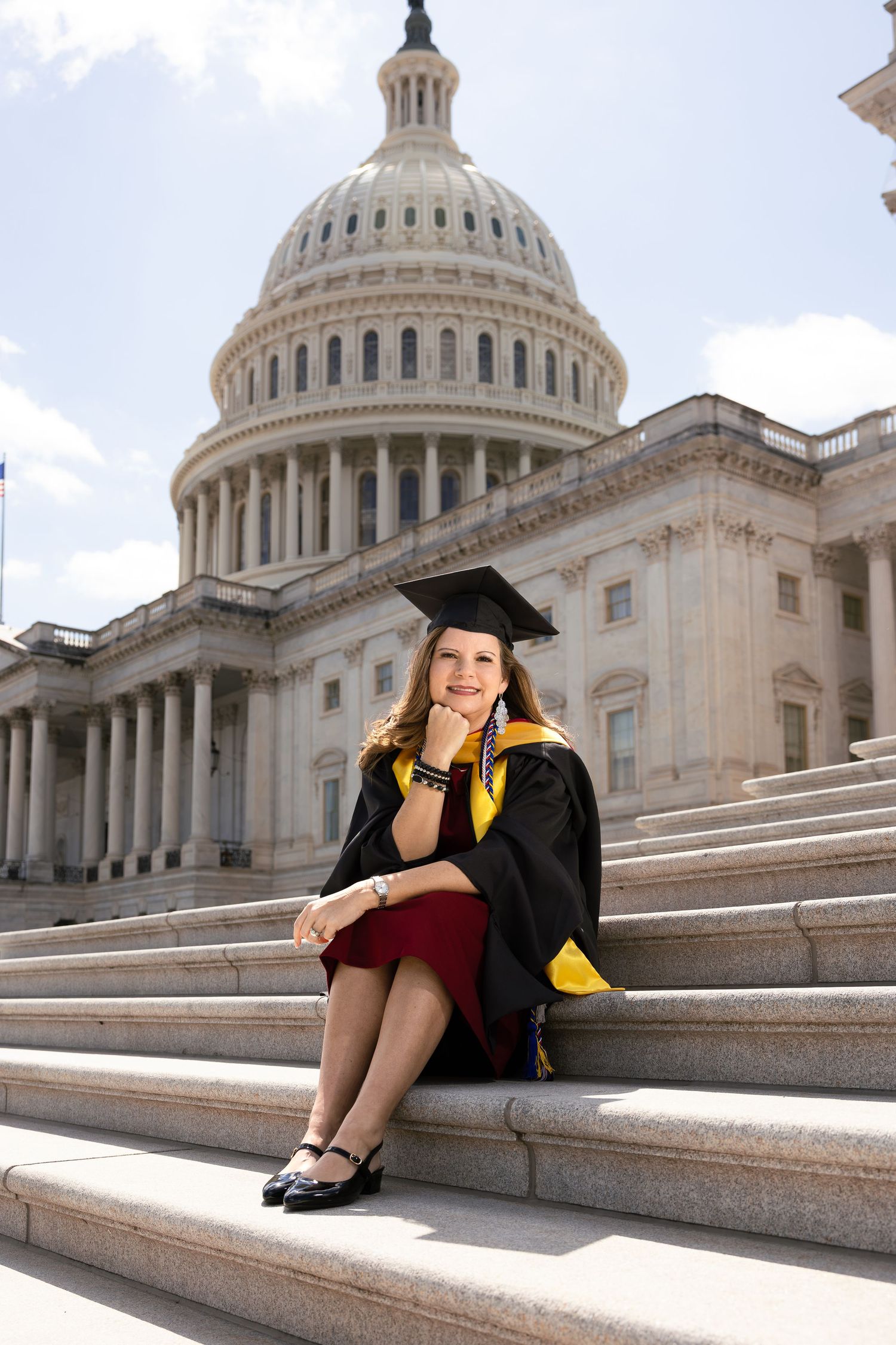 Graduate in cap and gown poses on the steps of the United States Capitol building in Washington DC.
