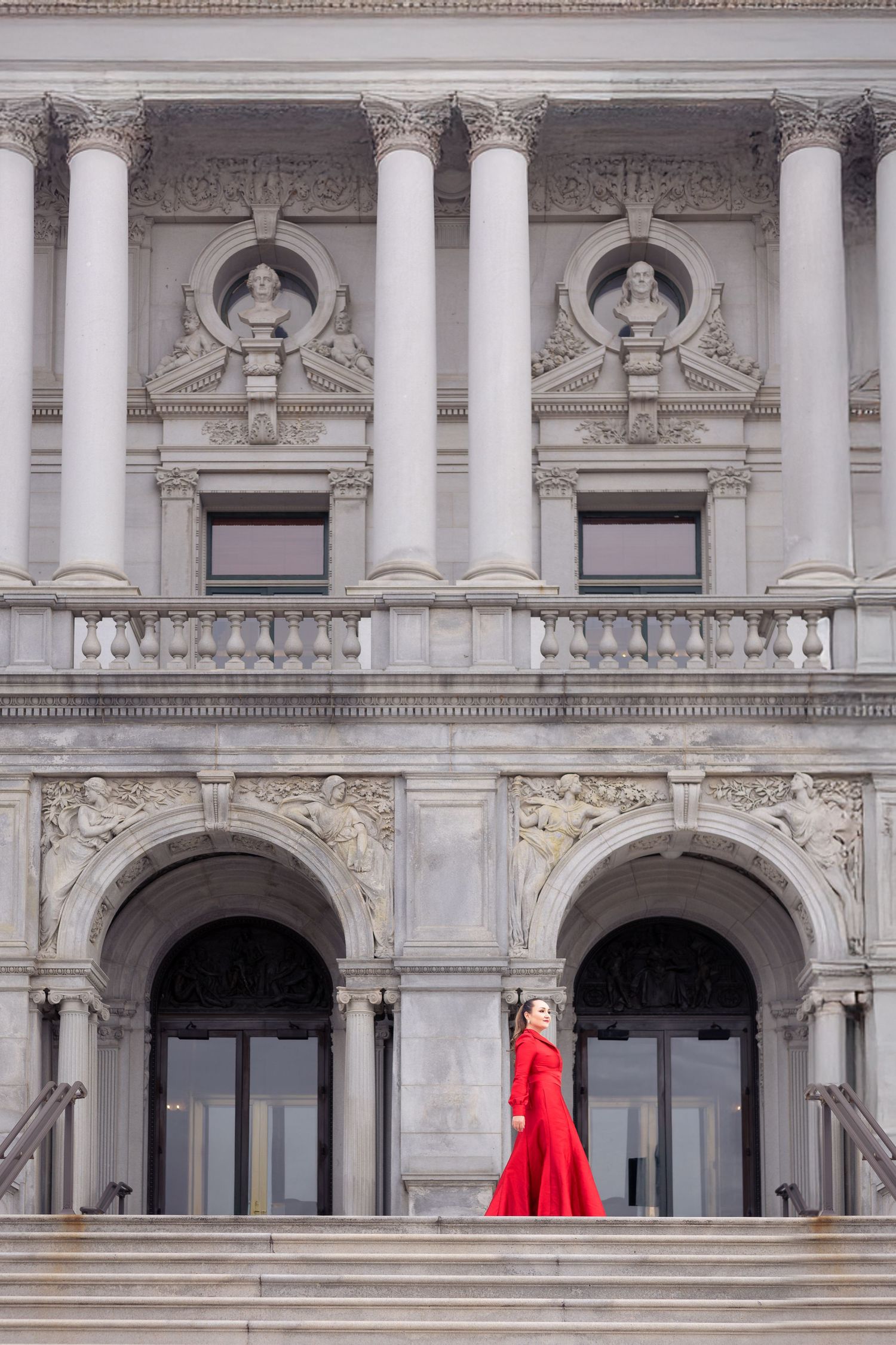 Dramatic red gown contrasts against classical white columns of historic government building.