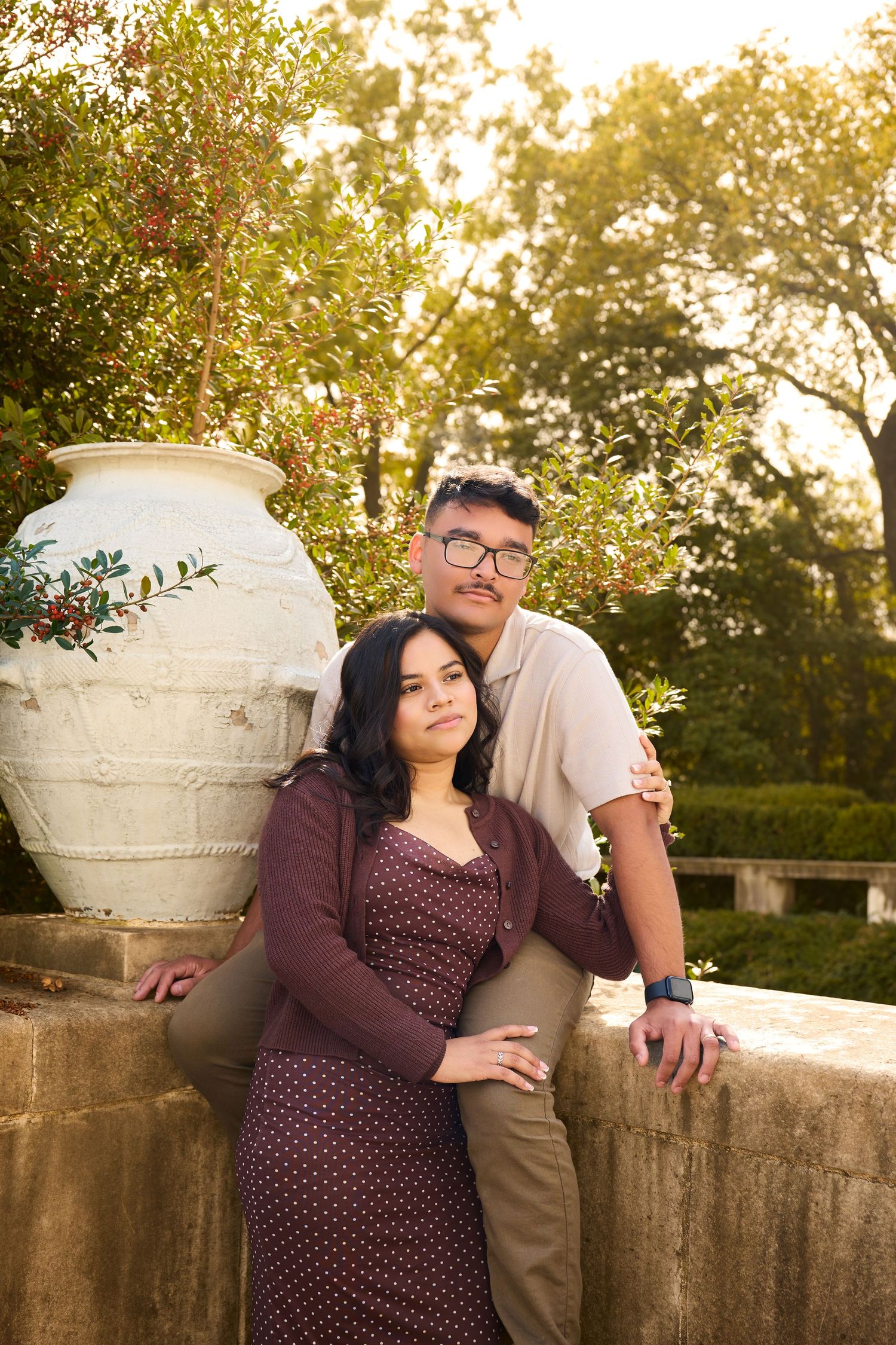 A couple poses together during a sunset photoshoot in a garden setting with decorative stone urns and warm lighting.
