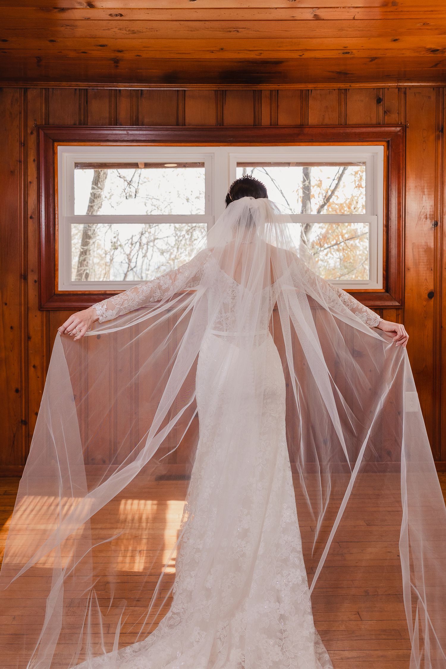 A flowing white wedding veil dramatically spread across a sunlit wooden floor with windows in the background.