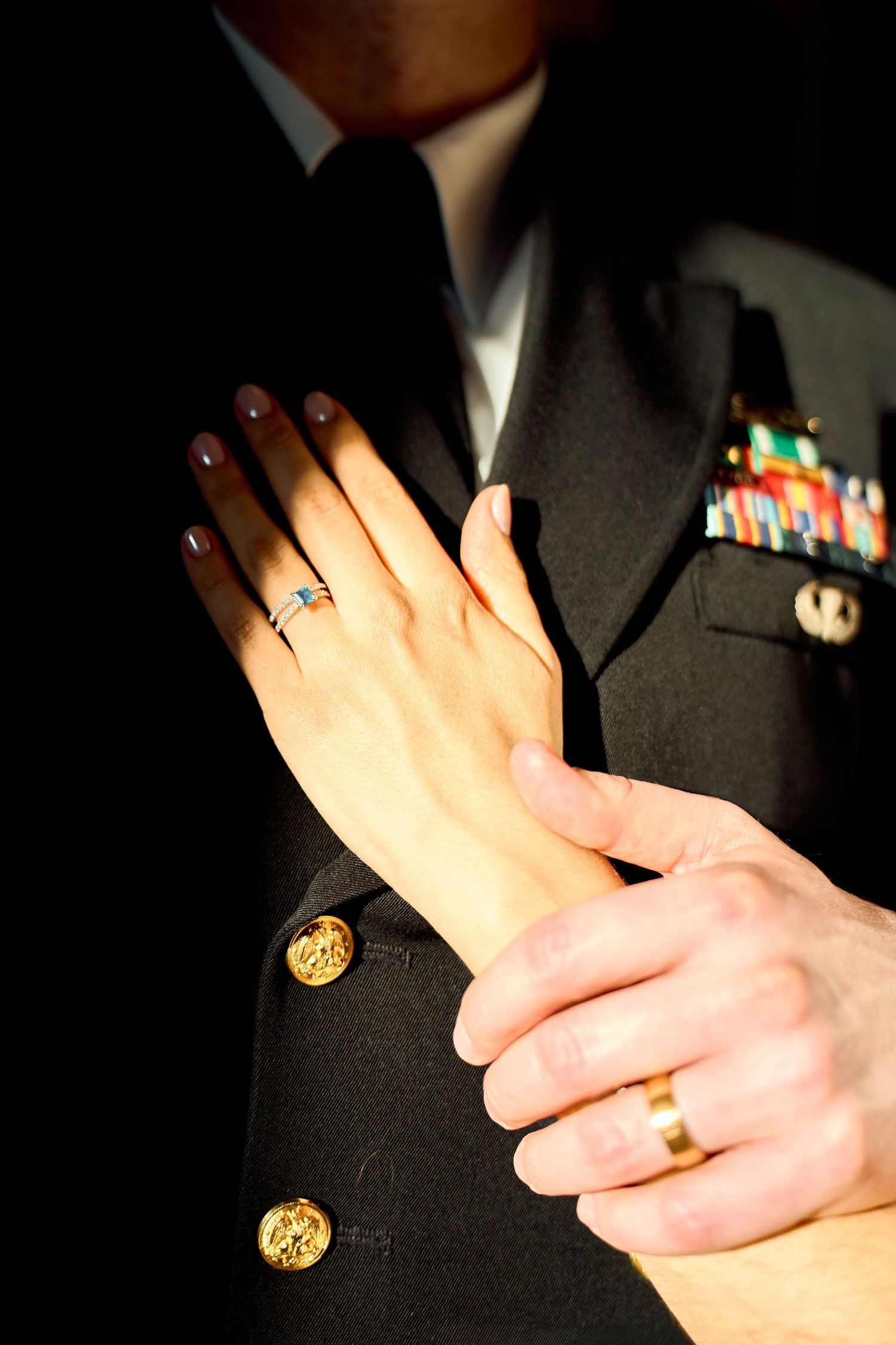 Military couple's hands showing wedding rings, man in dress uniform with ribbons and gold buttons.