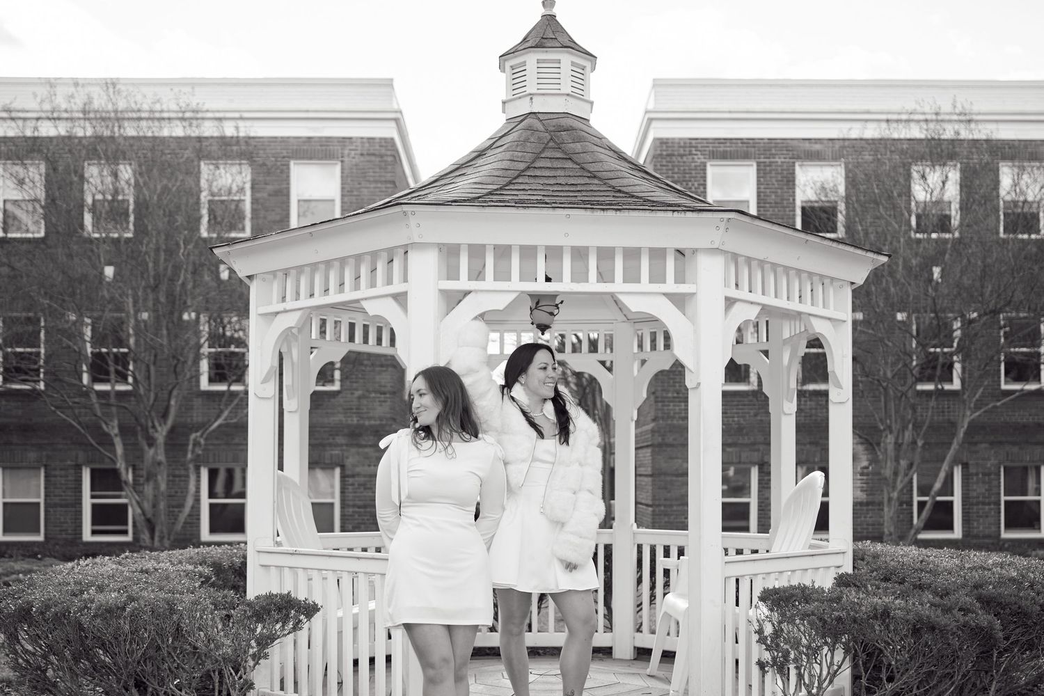 A row of white gazebos and brick buildings line a college campus walkway in black and white photography.