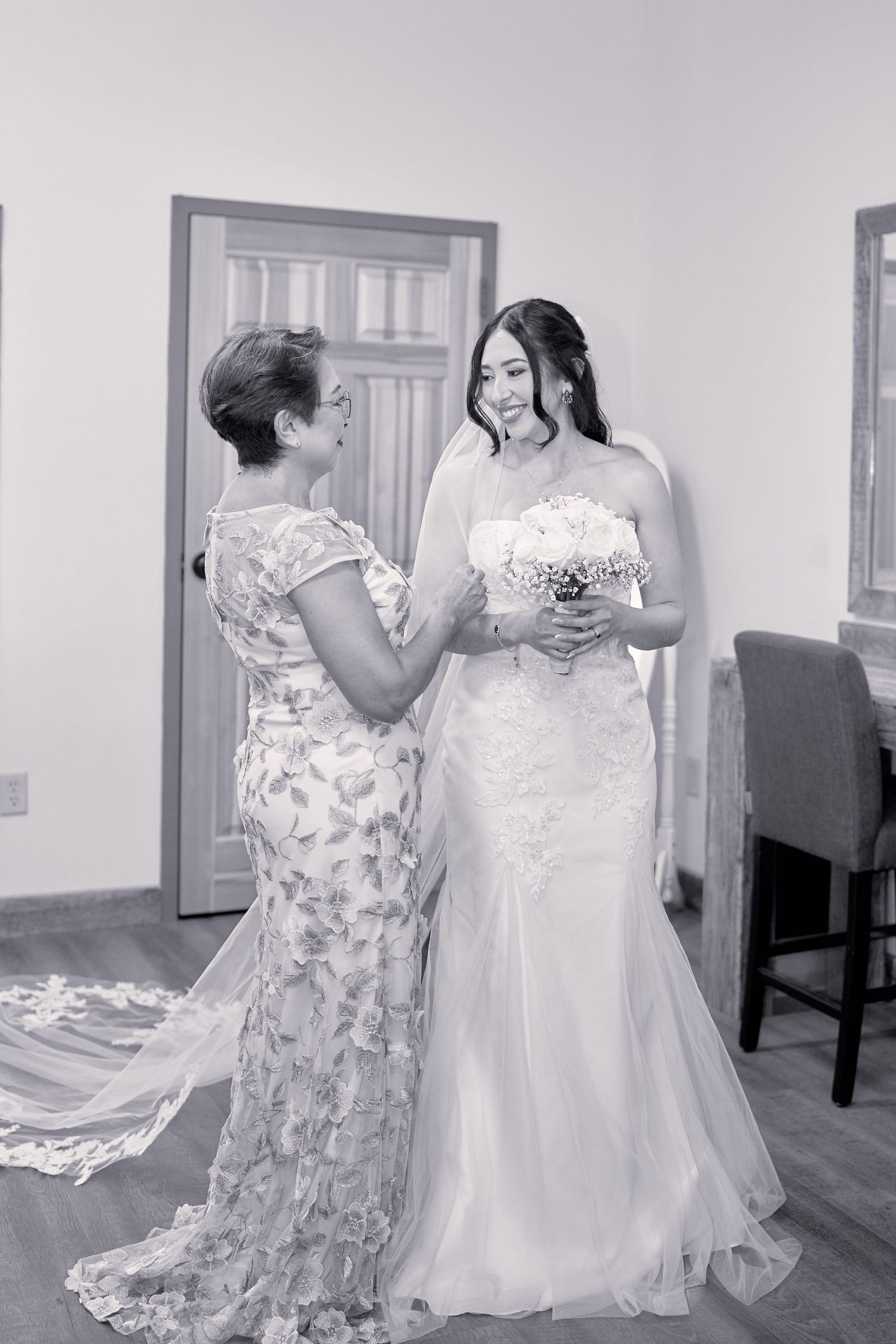 A touching black and white moment between two women in elegant gowns during wedding preparations.