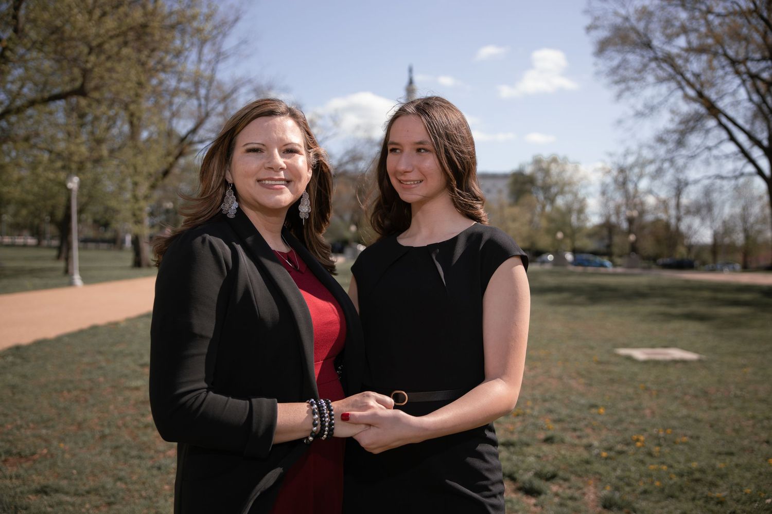Two people pose together in a park on a sunny day wearing black and red outfits.