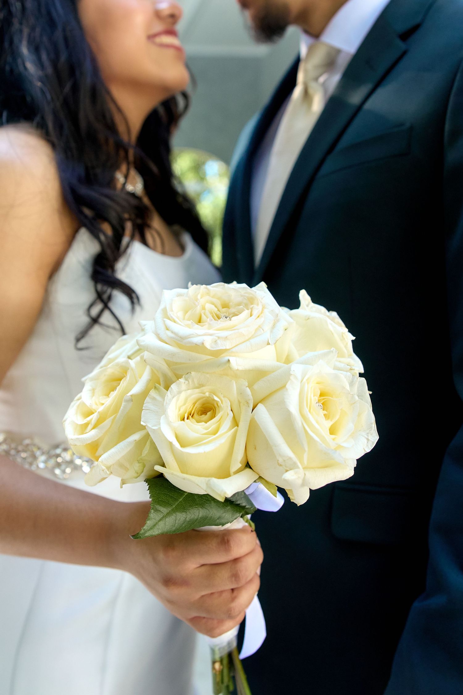 White rose bouquet held by bride in white dress next to groom in dark suit.