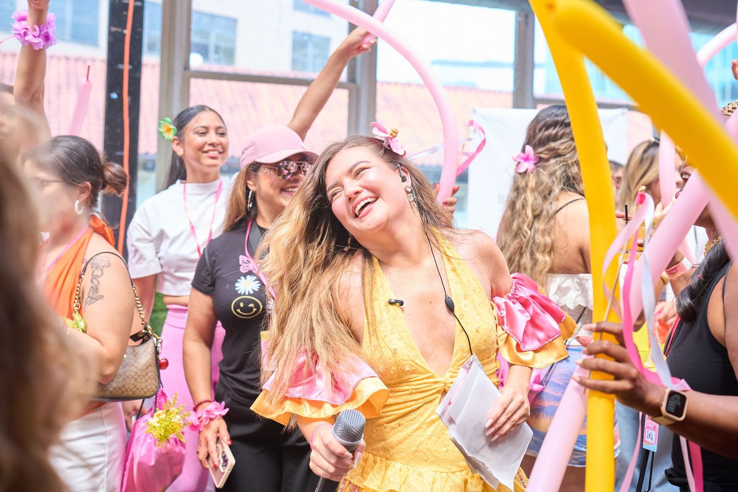 Excited woman in yellow dress laughing and dancing at a colorful outdoor celebration with balloons.