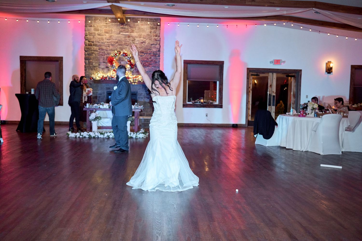 Bride celebrates on illuminated dance floor at wedding reception with pink ambient lighting.