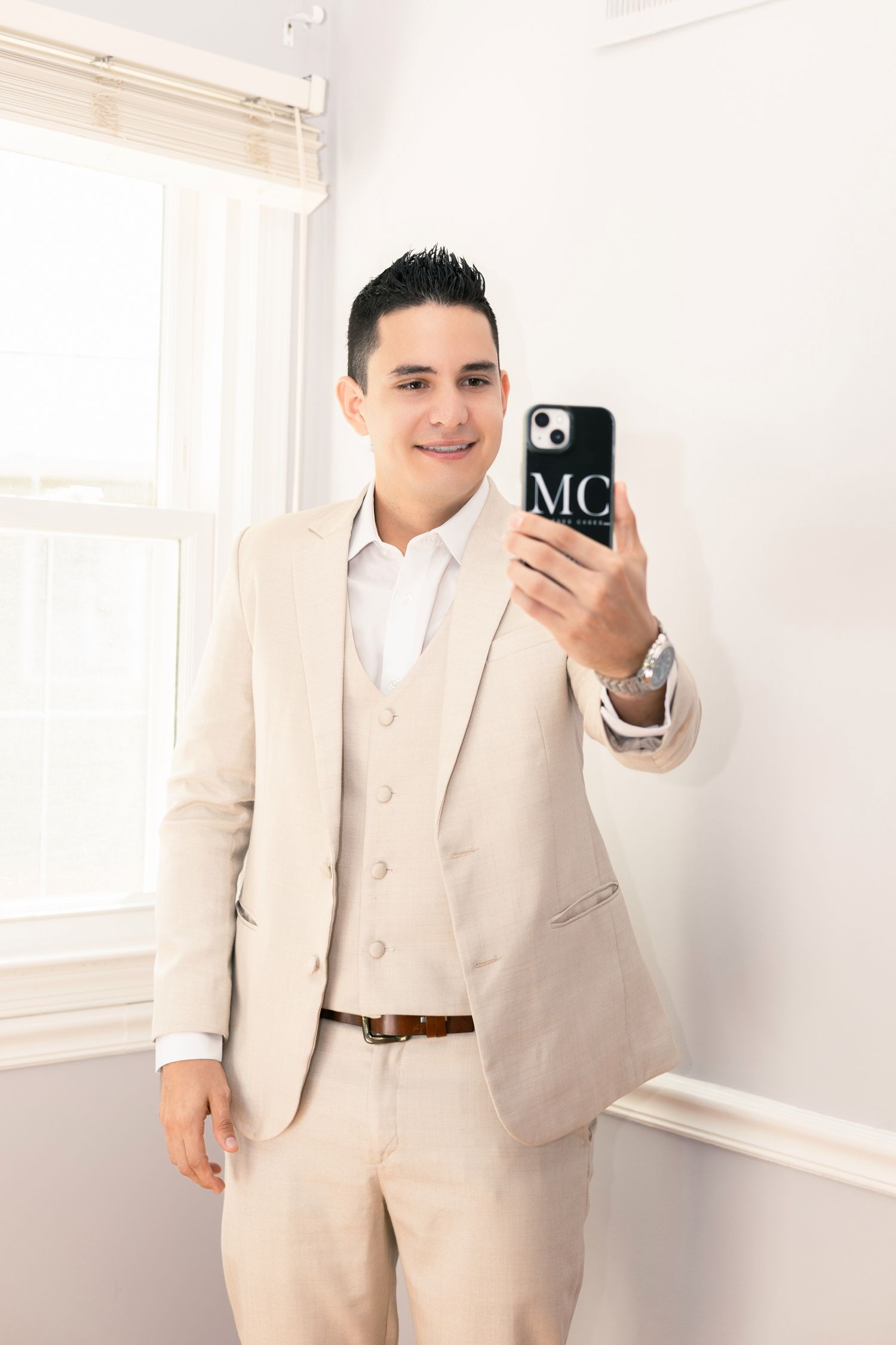 A person wearing a beige suit takes mirror selfies showing different poses and angles in a bright white room.