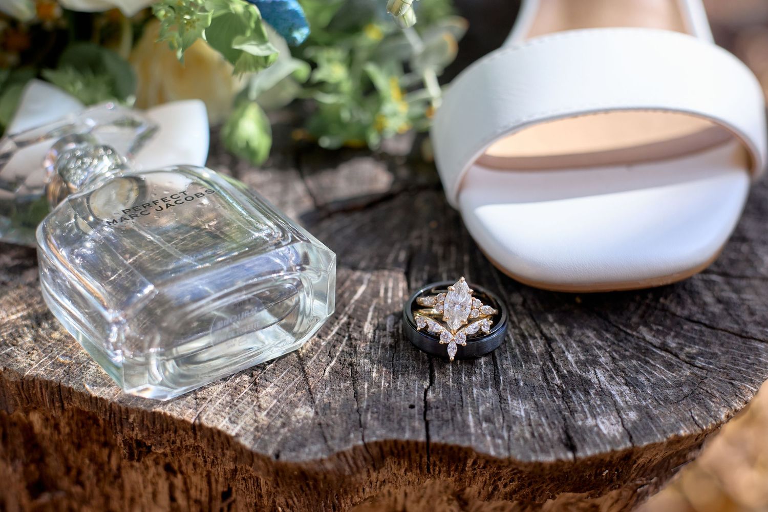 Wedding details including rings, perfume bottles, and delicate accessories arranged on rustic wooden surfaces.