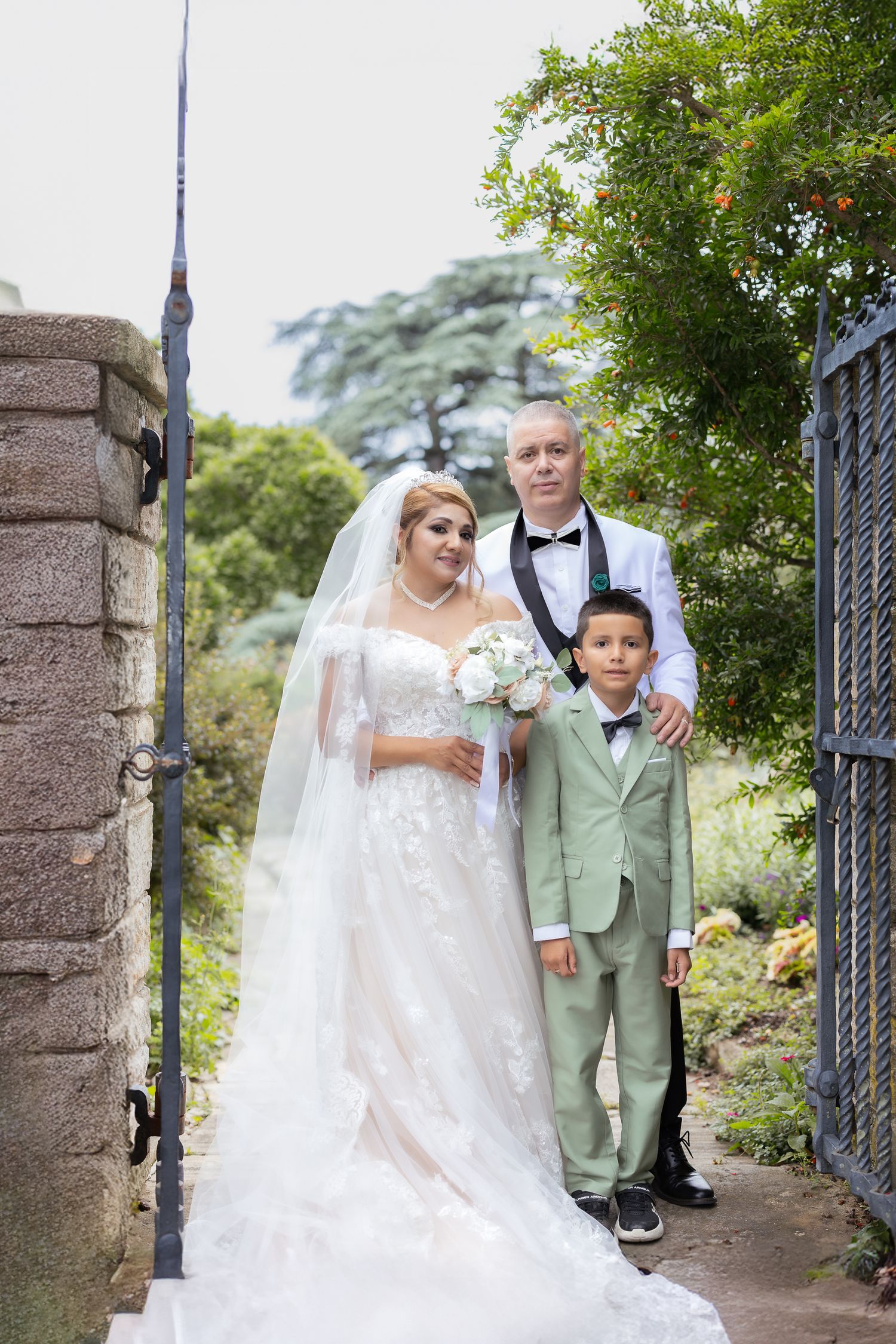A wedding couple stands elegantly at a stone gateway entrance surrounded by lush greenery on their special day.