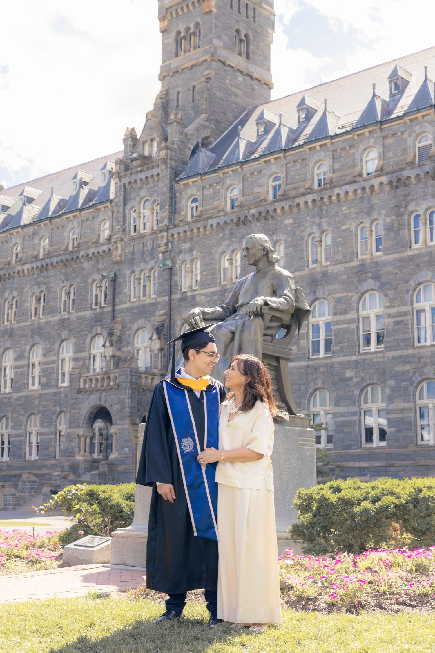A graduation photo taken in front of a grand Gothic revival university building with dormer windows and ornate architecture.