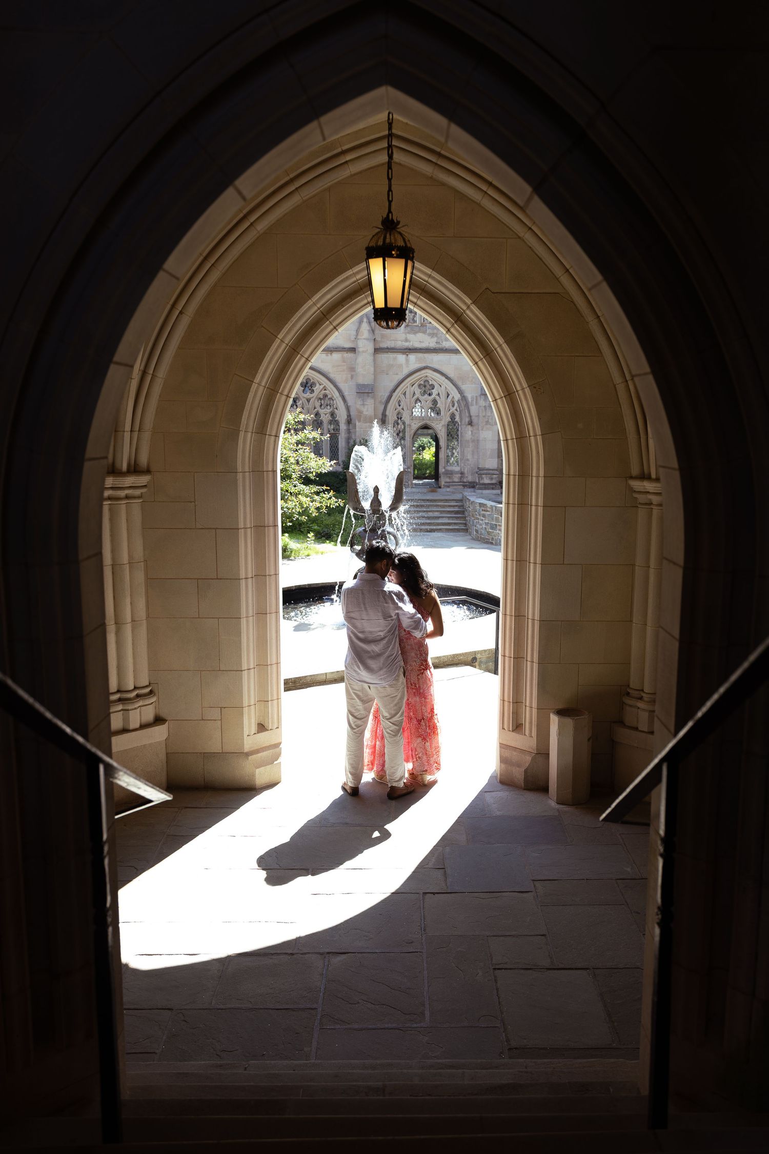 Silhouetted figures stand in a Gothic stone archway with light streaming through, casting dramatic shadows.