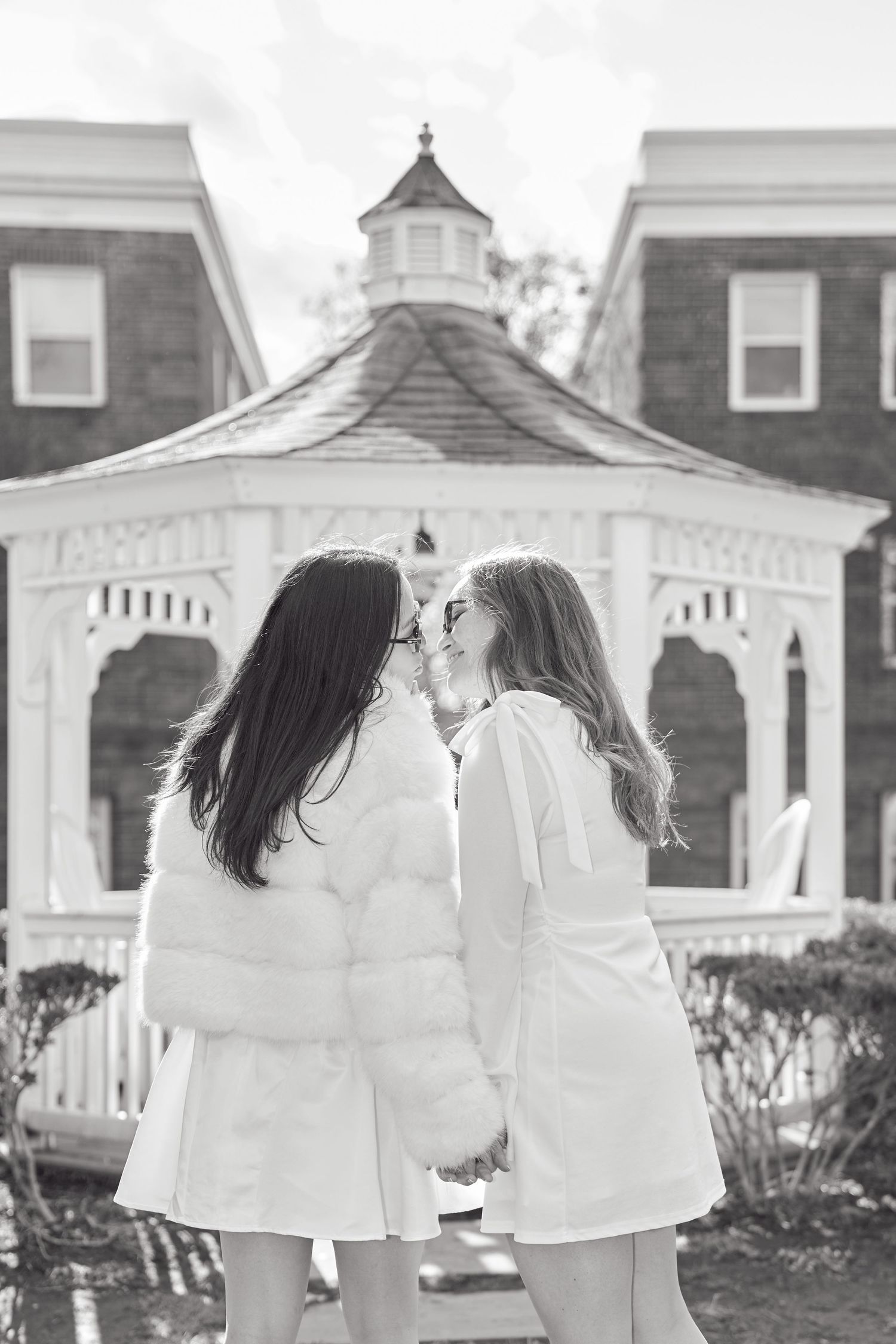 A black and white photo of people in white dresses standing near gazebos and brick buildings.