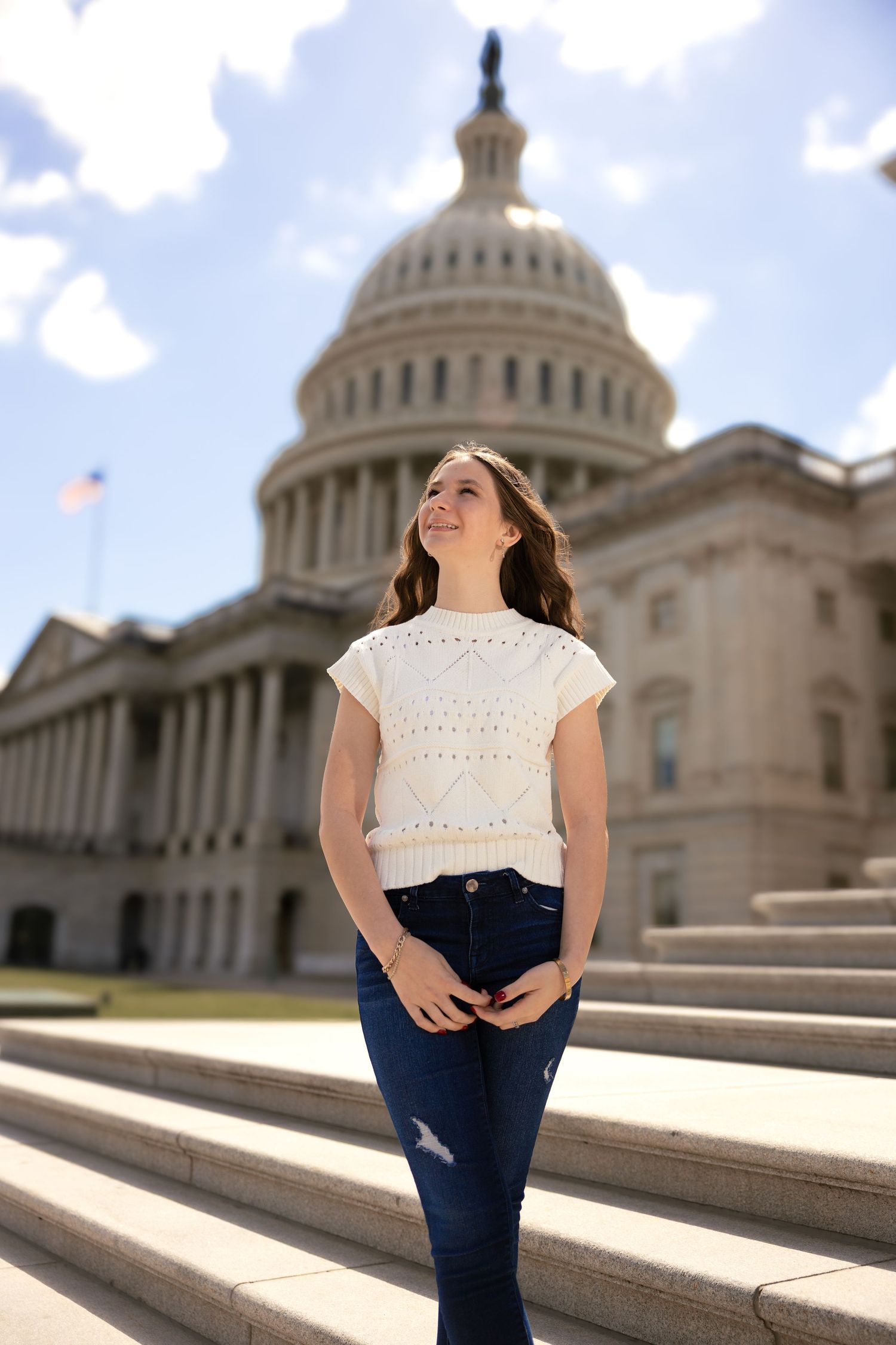 A person wearing a white crochet top and jeans poses on the steps of the U.S. Capitol building in Washington DC.