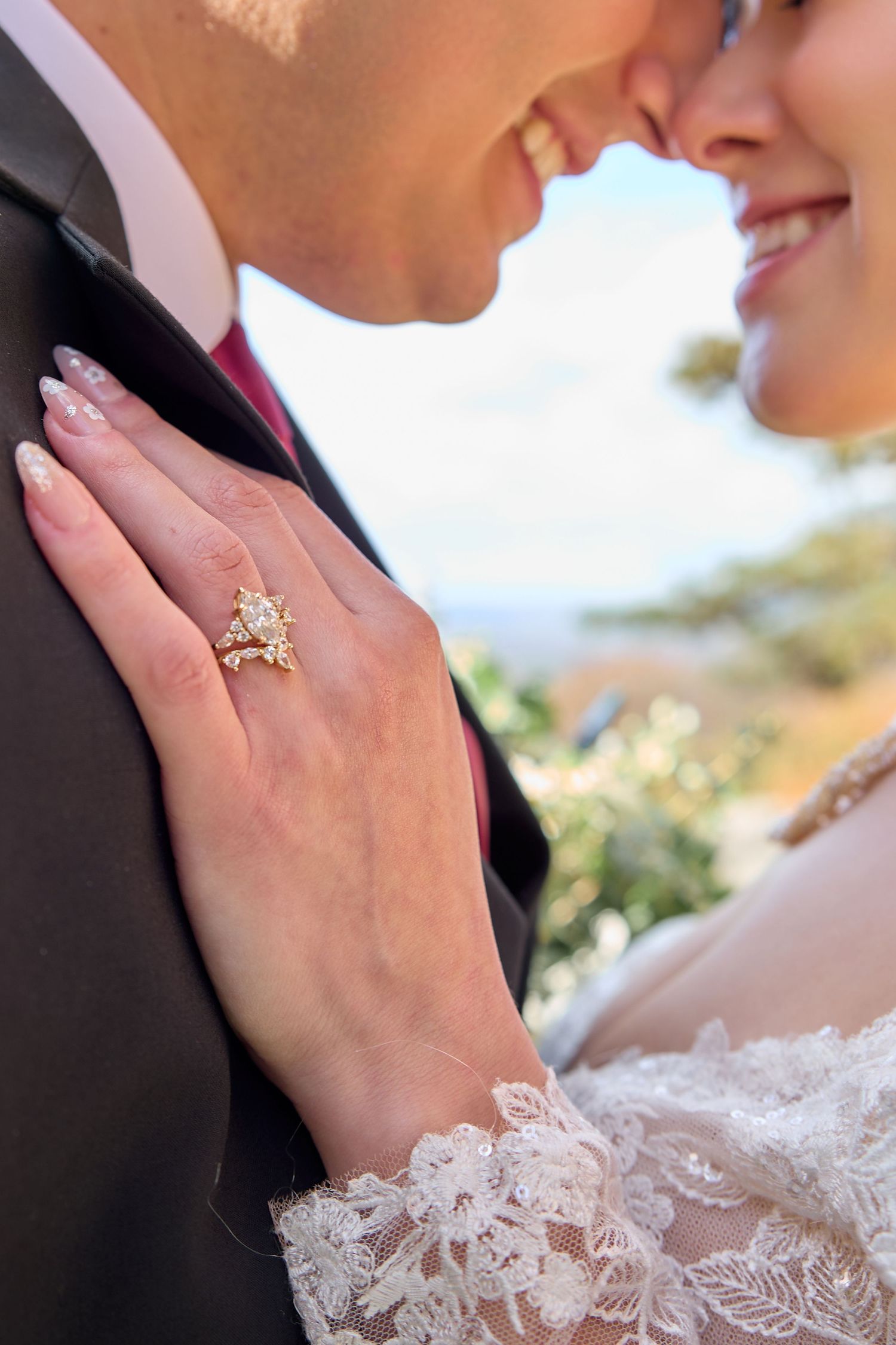 Close up of a bride's hand with engagement ring resting gently on groom's face during an outdoor wedding portrait.
