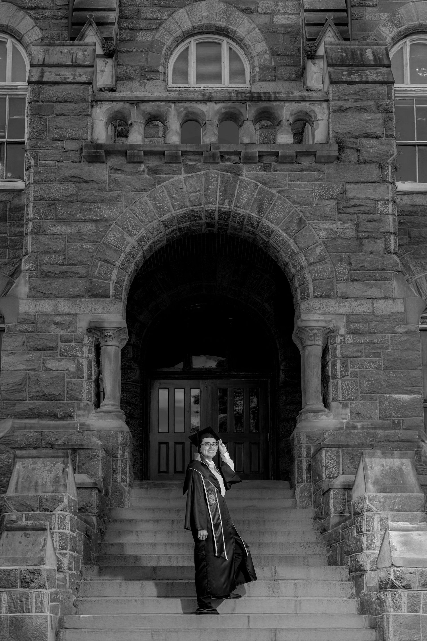 Figure stands in black winter coat on stone steps beneath Gothic archway entrance of historic university building.