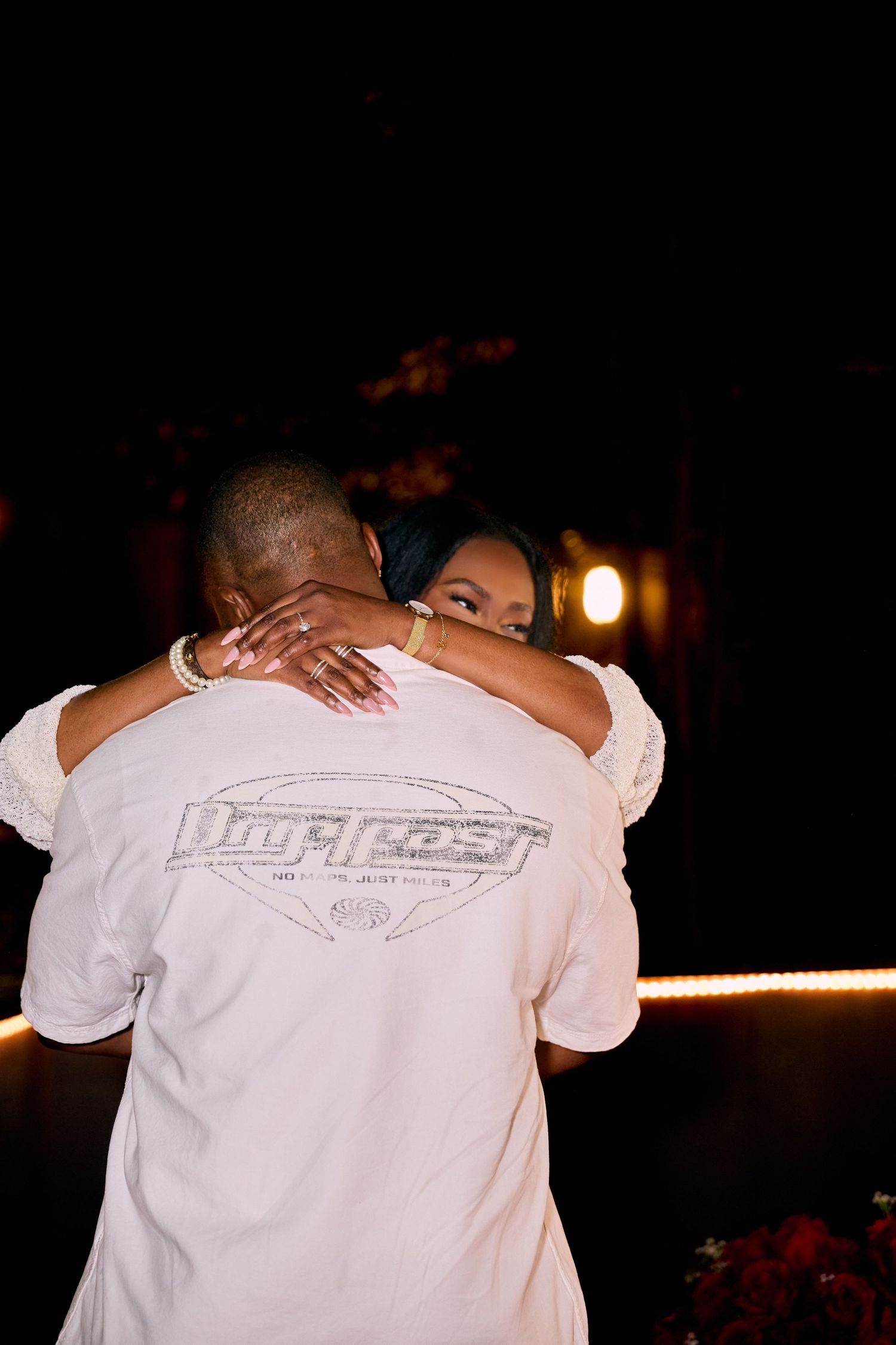 A tender embrace captured during a nighttime celebration with string lights in the background.