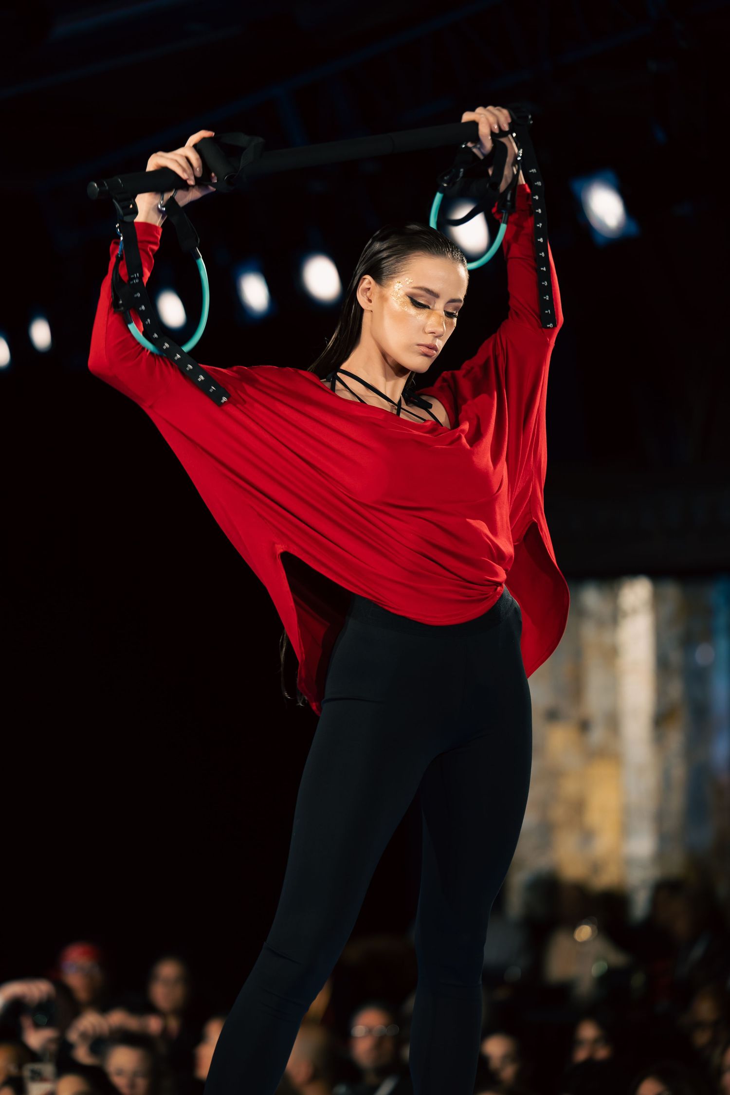 Model in flowing red top and black leggings poses dramatically with headphones on runway.