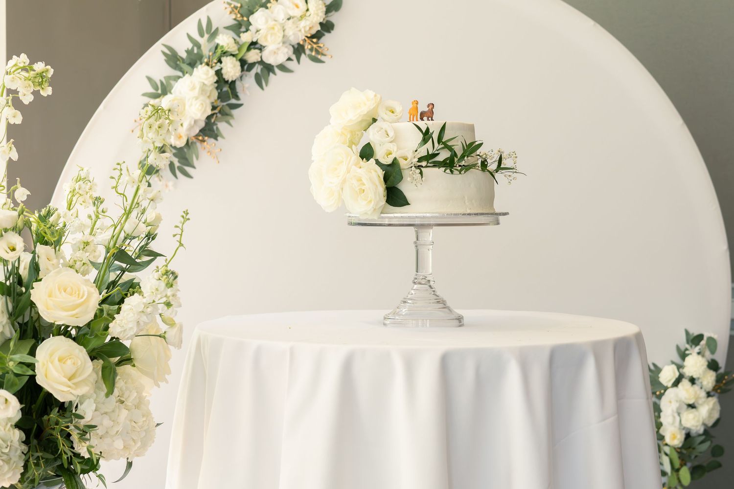 White floral centerpieces with roses and greenery decorate elegant round tables at a formal wedding reception.
