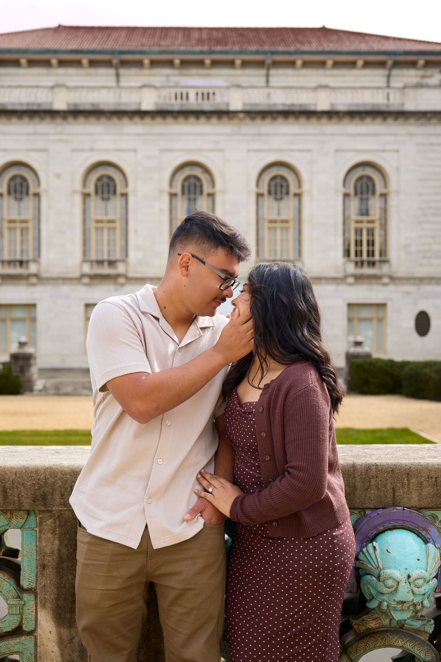 A couple shares an intimate moment against the backdrop of a historic building with arched windows.
