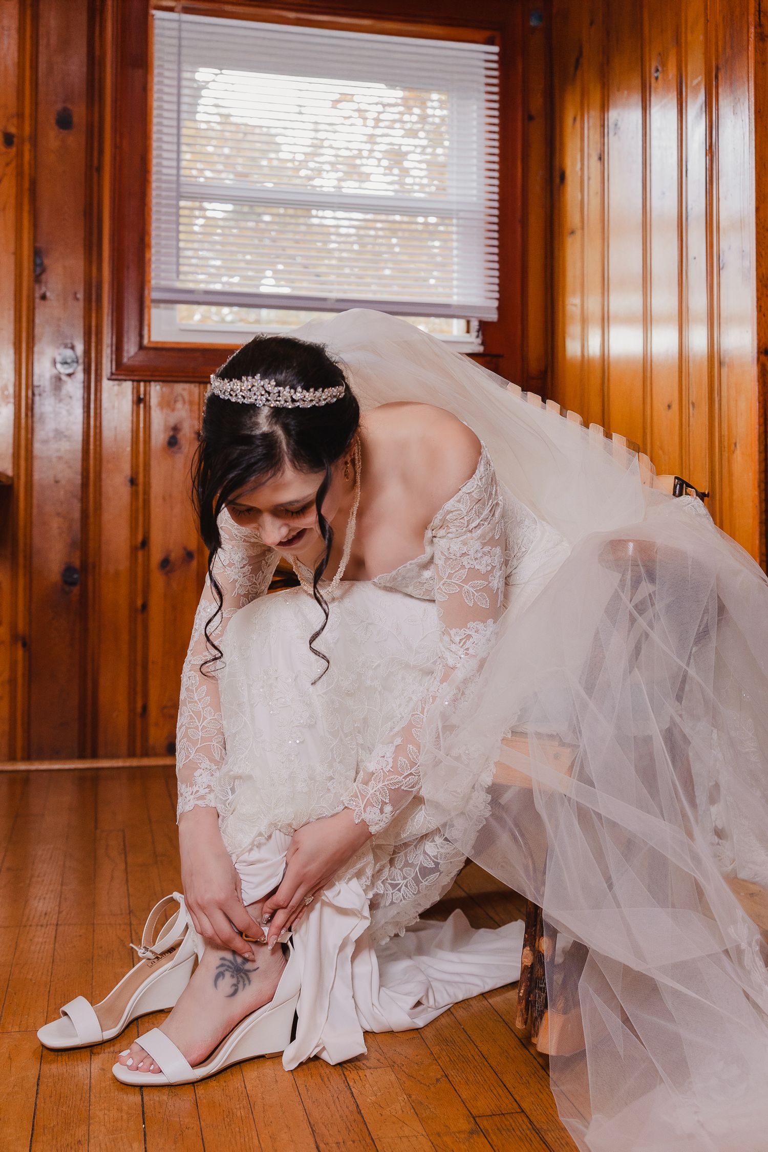 Close-up shots of a bride in a lace wedding dress putting on white bridal shoes on a wooden floor.