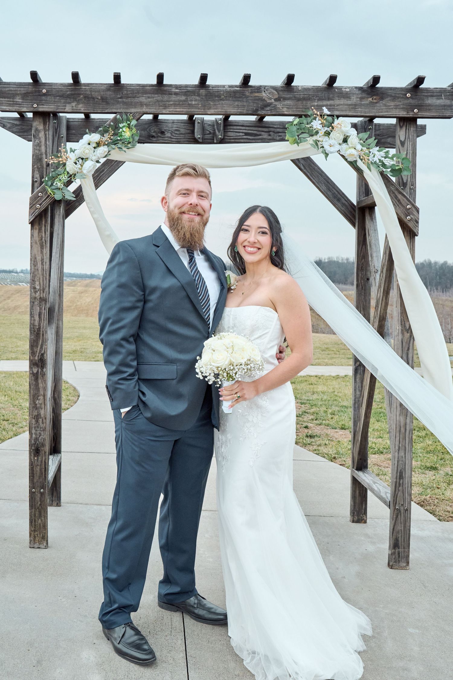 Newlyweds pose together under a rustic wooden pergola on their wedding day.