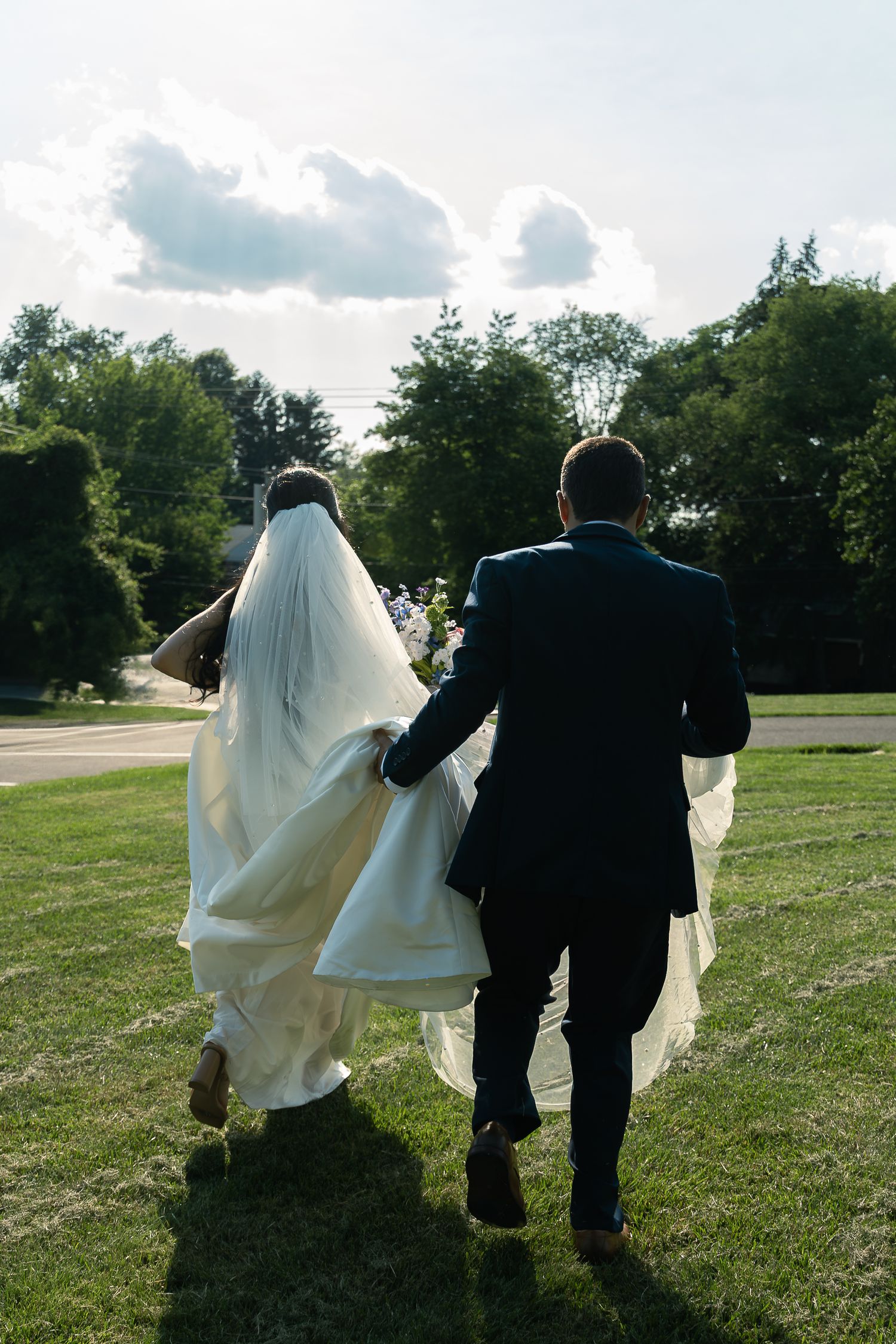 A couple in wedding attire walks together through a grassy field on their special day.
