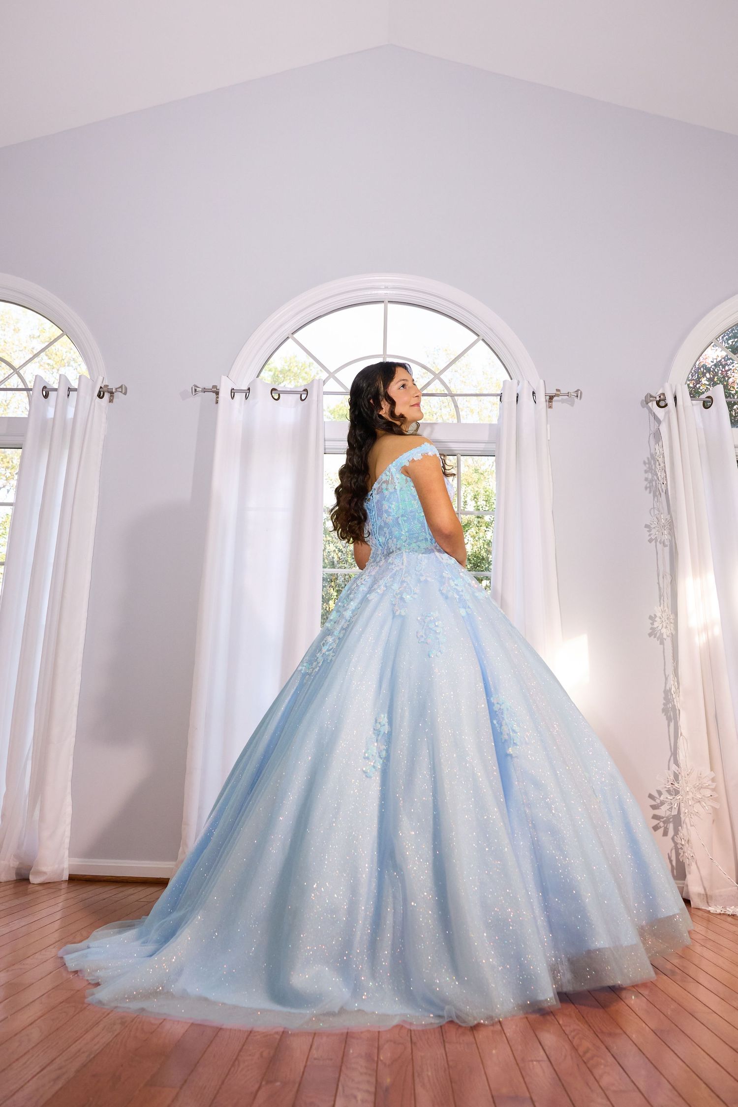 A flowing light blue ballgown with sparkly details photographed in an elegant white room with arched windows.