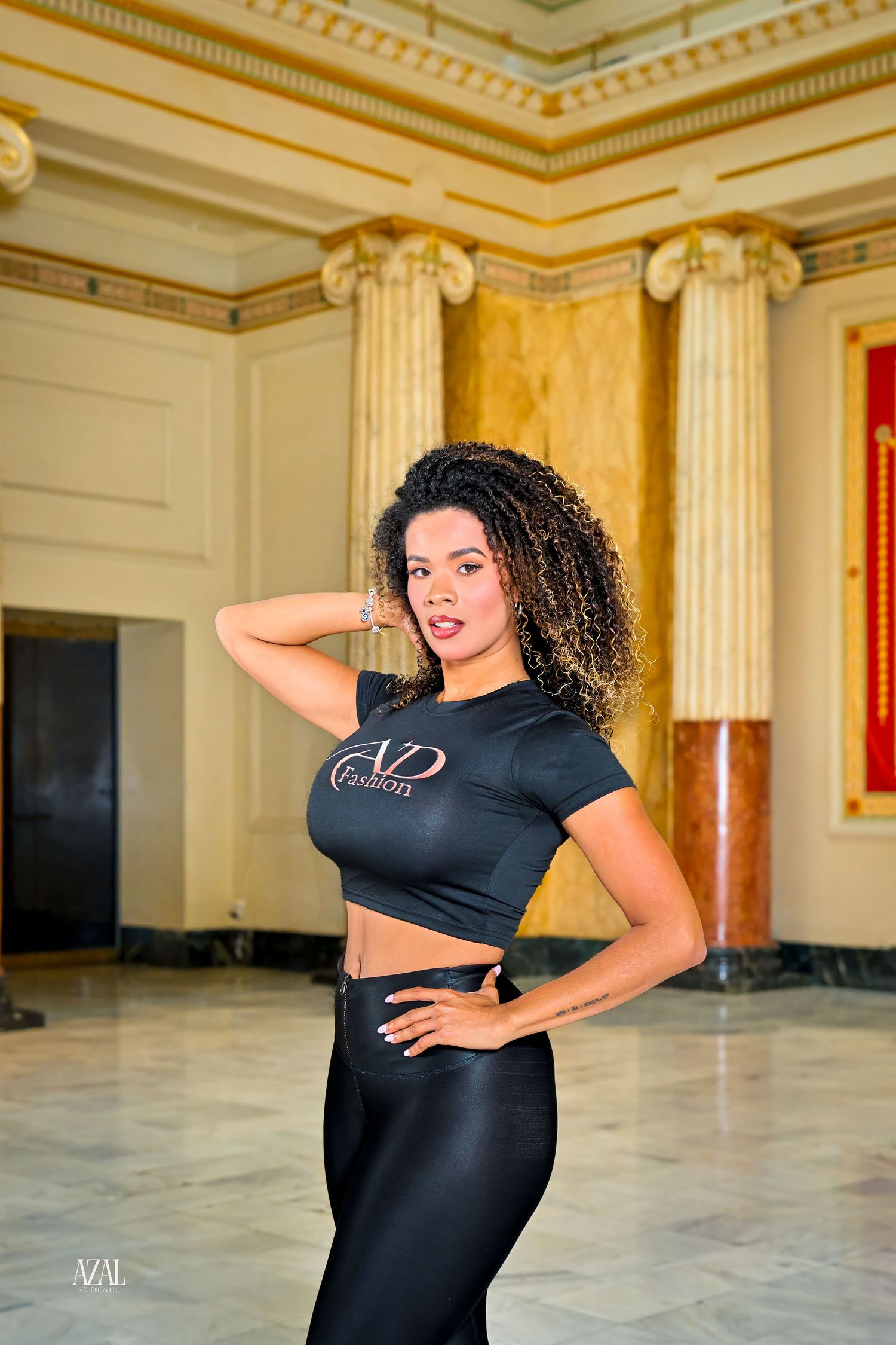 Woman in black crop top and leggings poses confidently in elegant hall with marble columns.