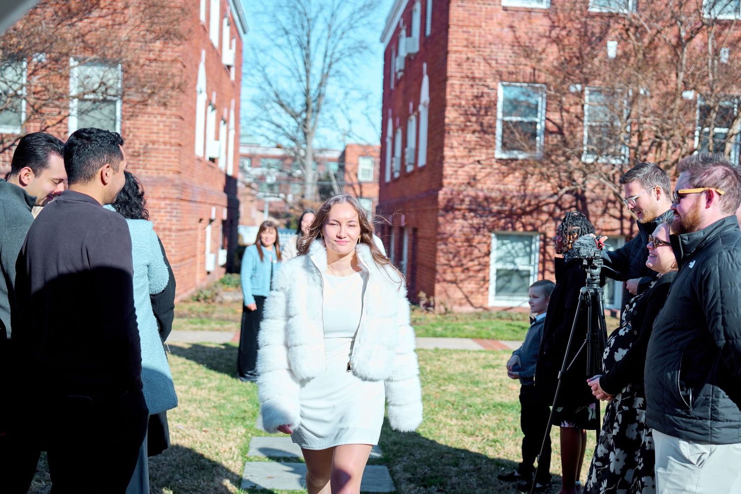 A group of people gather outdoors near brick buildings on a sunny day for a social event.