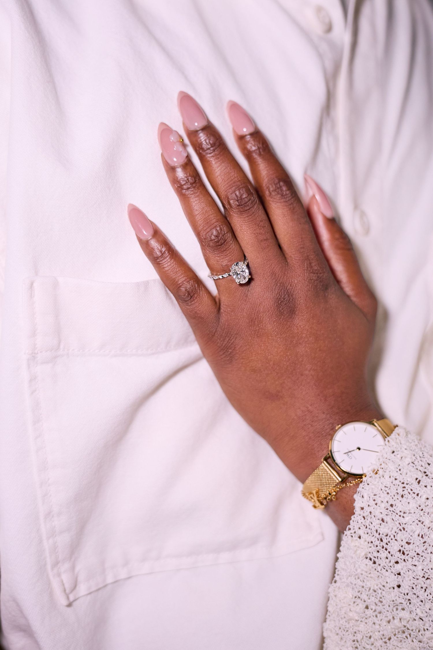 Close-up view of hands wearing engagement rings and delicate lace sleeves against white fabric background.