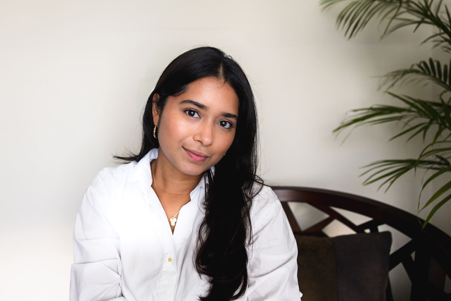 Professional headshot in white blouse against neutral background with indoor plant.