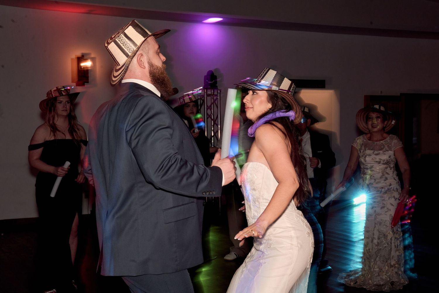 A couple dances together at their reception with colorful lights in the background.