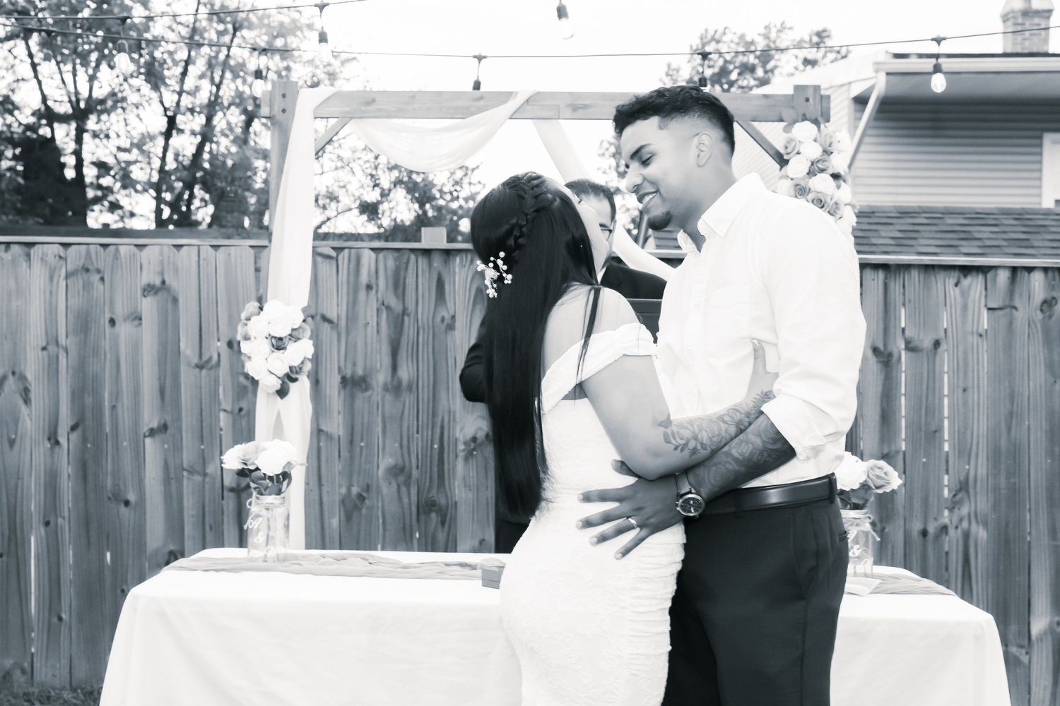 A romantic black and white wedding moment captured under a decorated arch in a backyard setting.