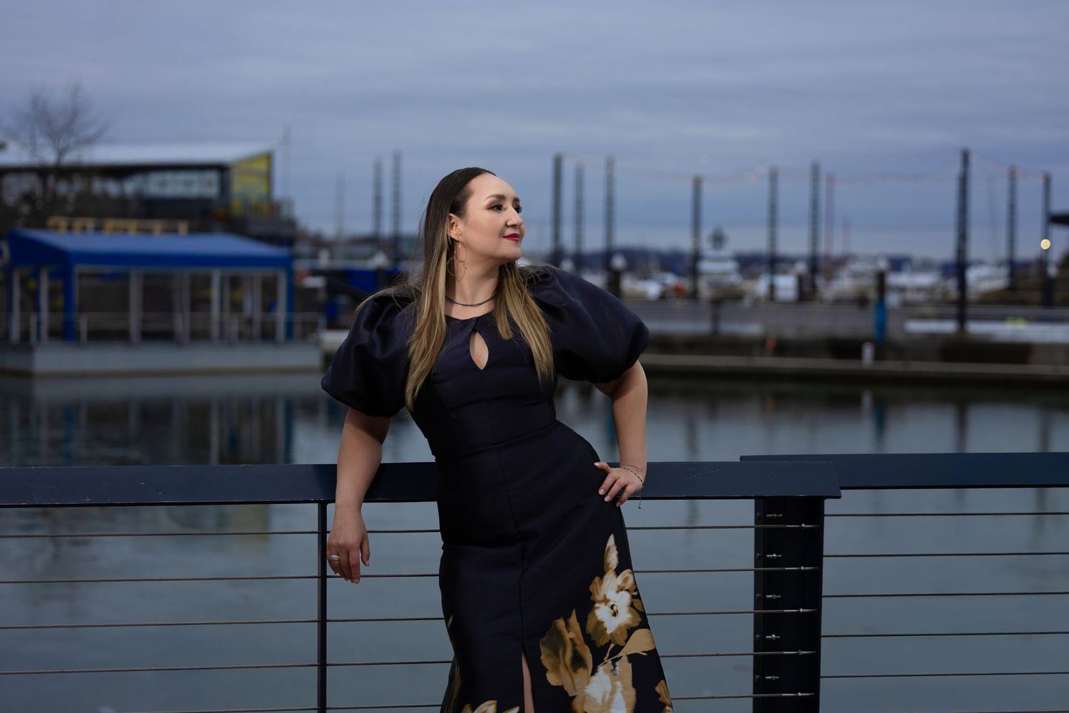 Elegant black dress with floral details photographed against waterfront marina at dusk.