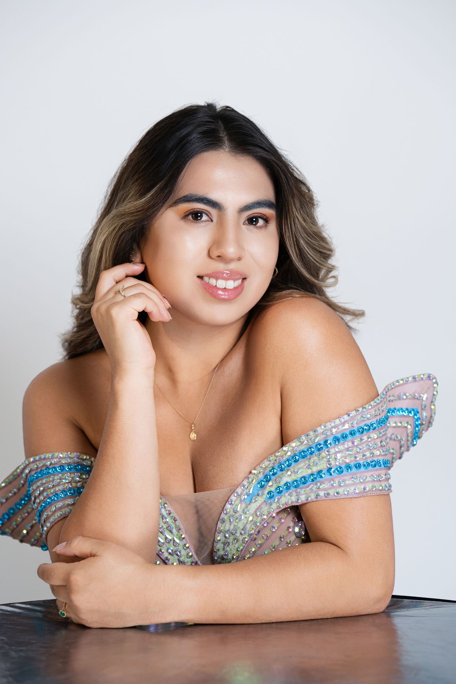 Young woman in a sparkling off-shoulder blue and silver embellished gown posing elegantly against a white background.