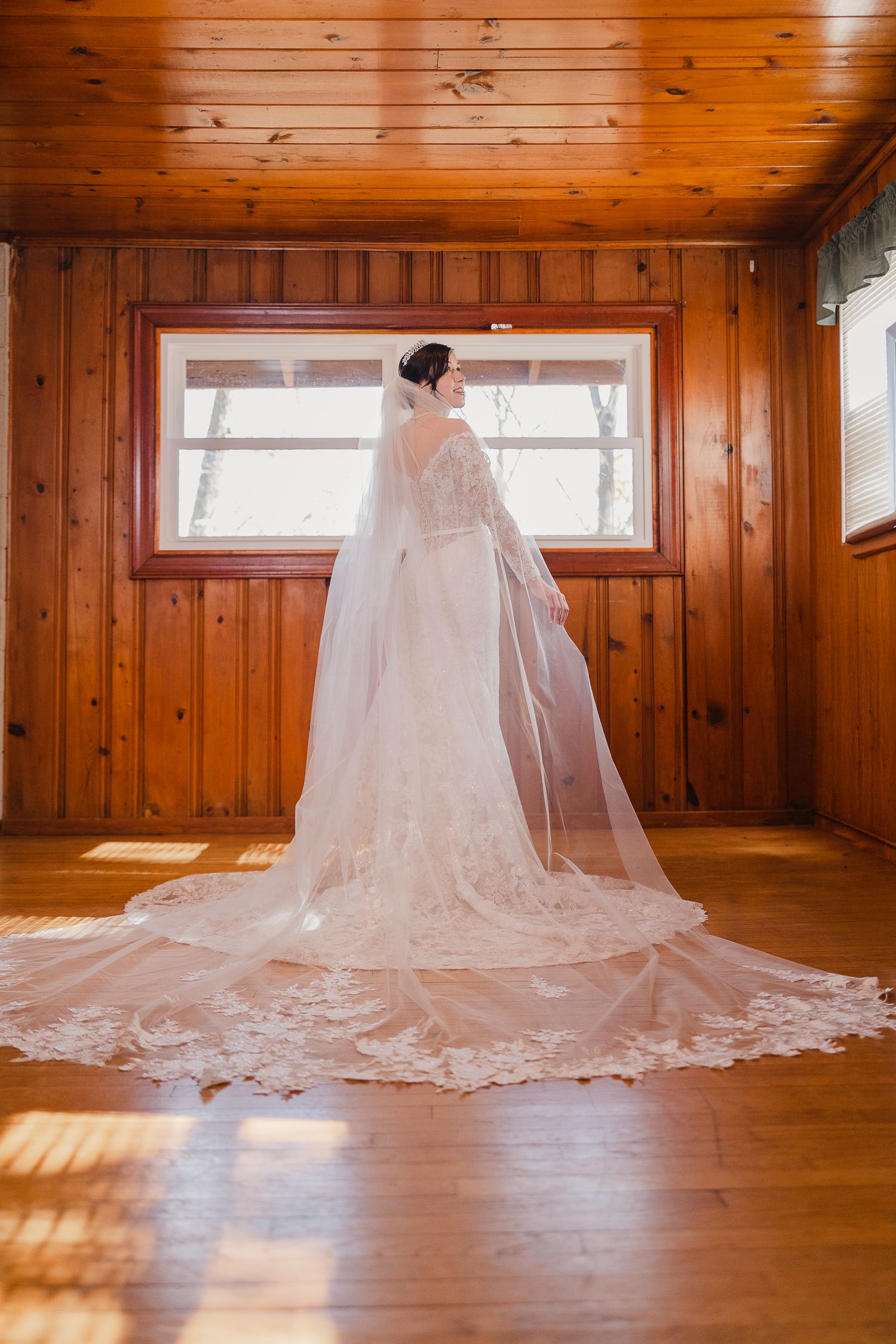 A flowing white wedding gown and veil spread elegantly across a sunlit wooden floor in a rustic room.