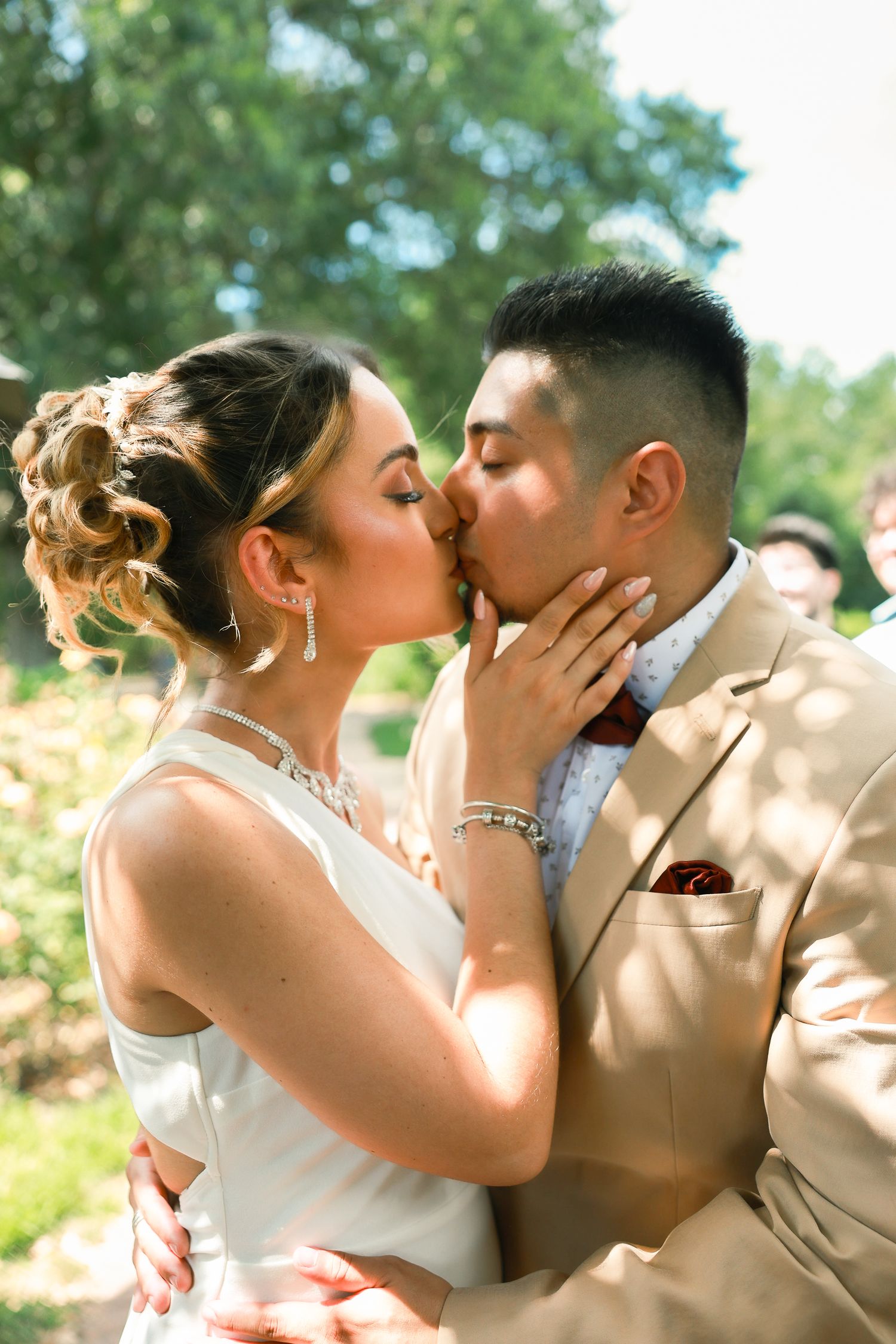 Romantic wedding kiss between bride in white dress and groom in tan suit in garden setting.