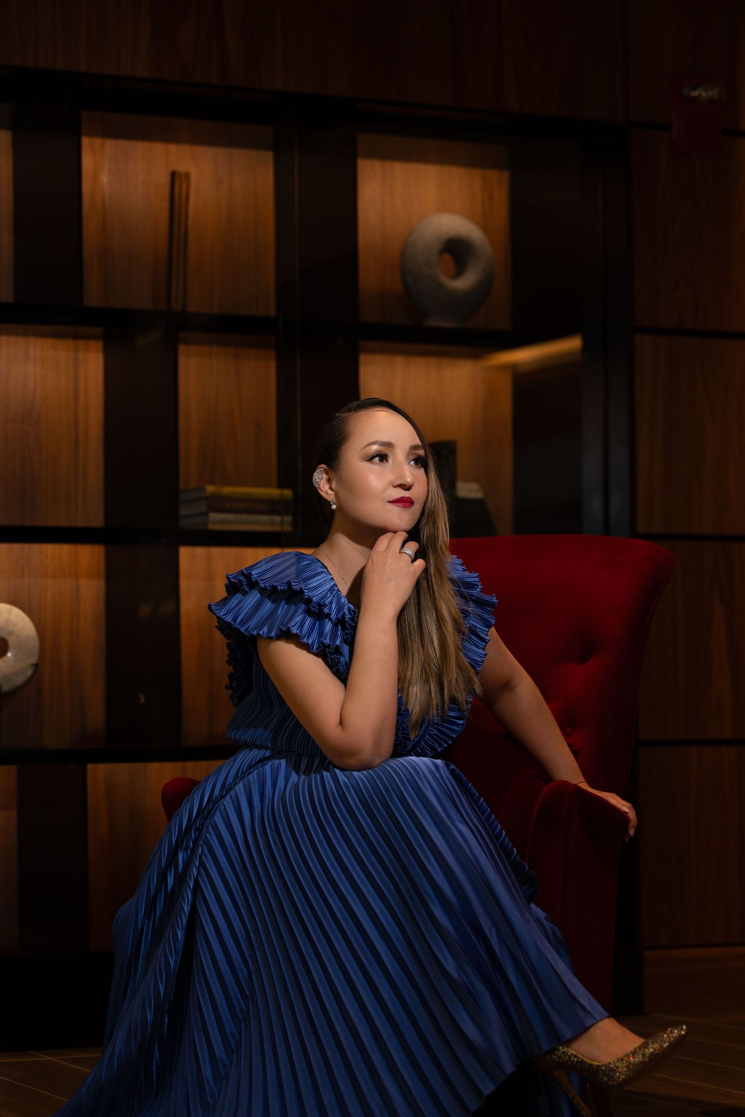 Woman in navy blue evening gown seated elegantly in modern interior setting.