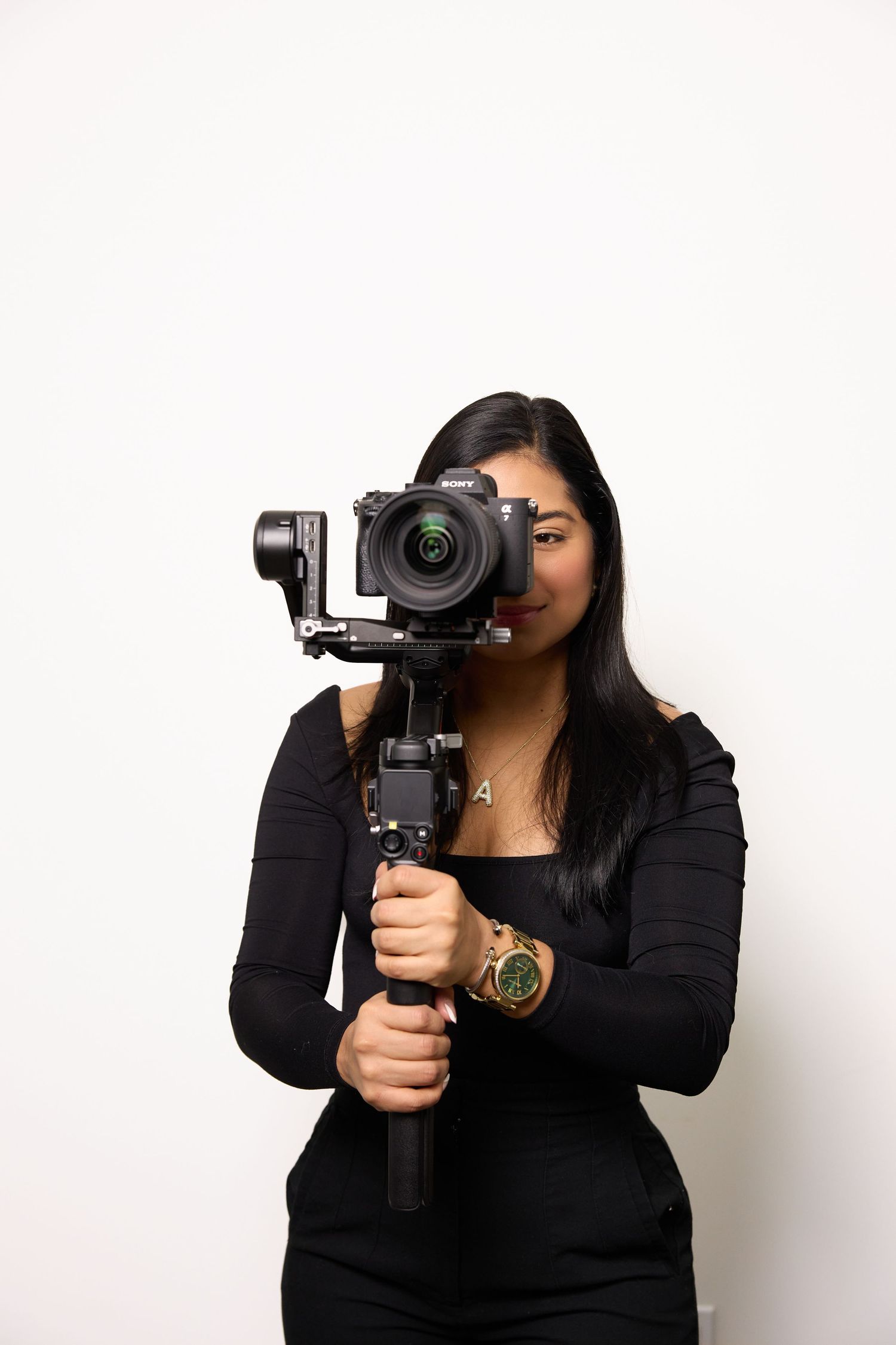 Professional photographer in black clothing holds video camera in different creative poses against white background.