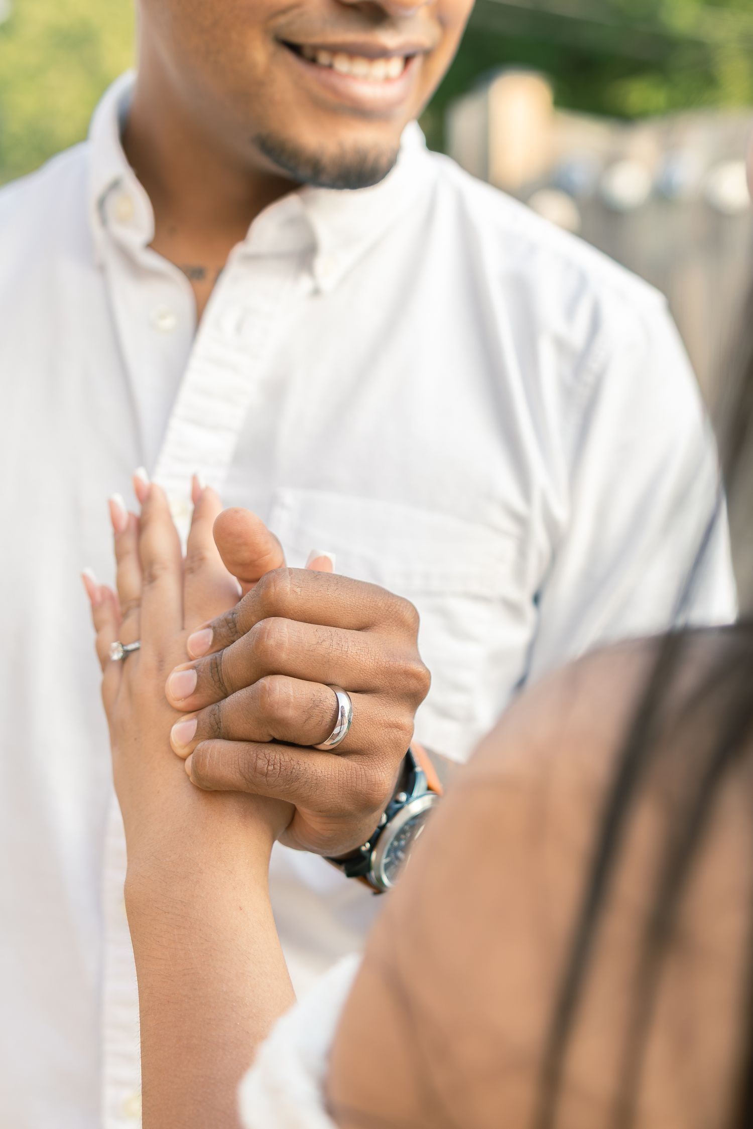 Close-up view of hands wearing wedding rings against a white clothing background.