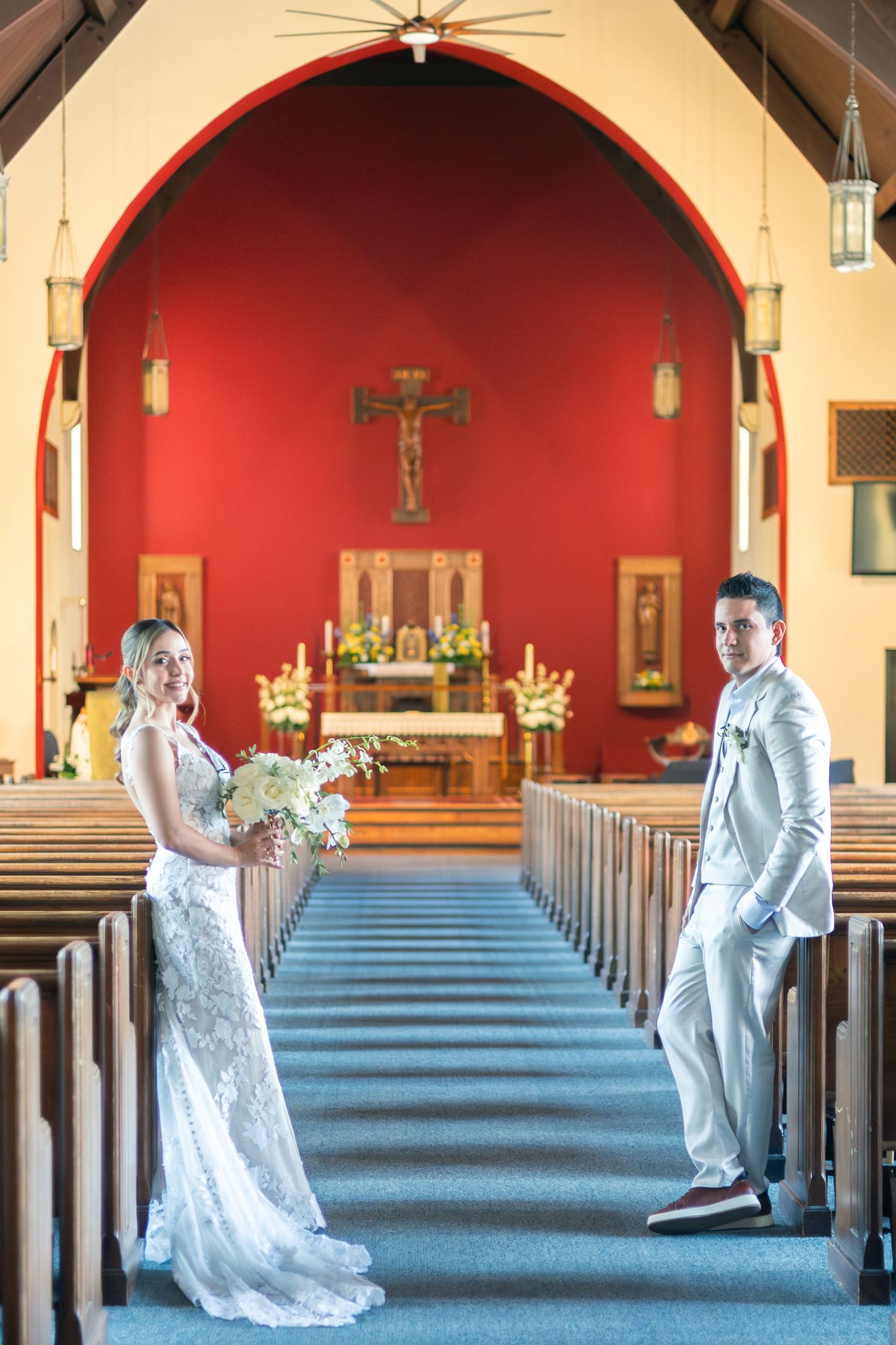 A wedding couple poses in a sequence of four photos inside a church with red arched walls and blue carpeted aisle.