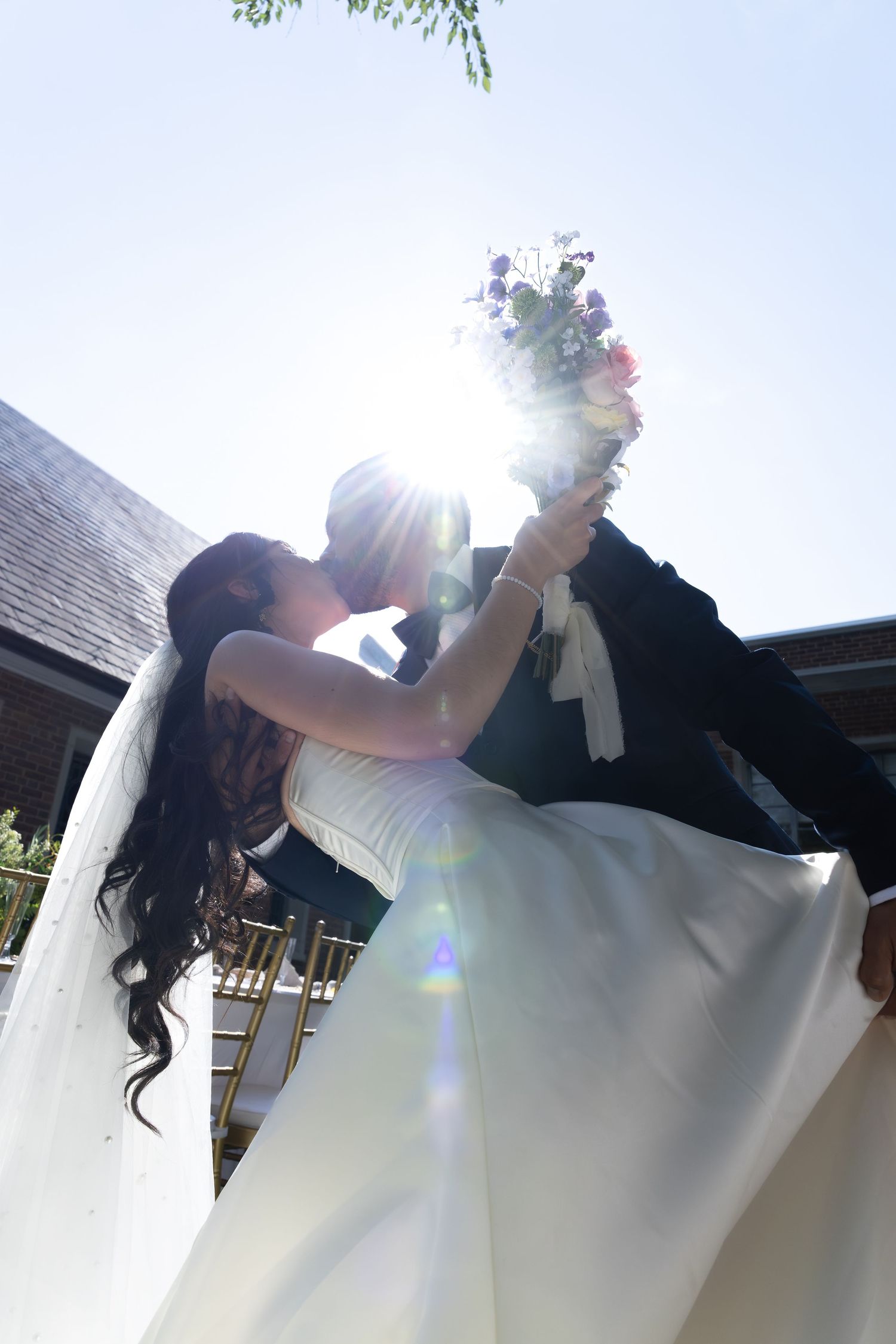 A couple in wedding attire dancing together outdoors with sunlight creating a beautiful lens flare.