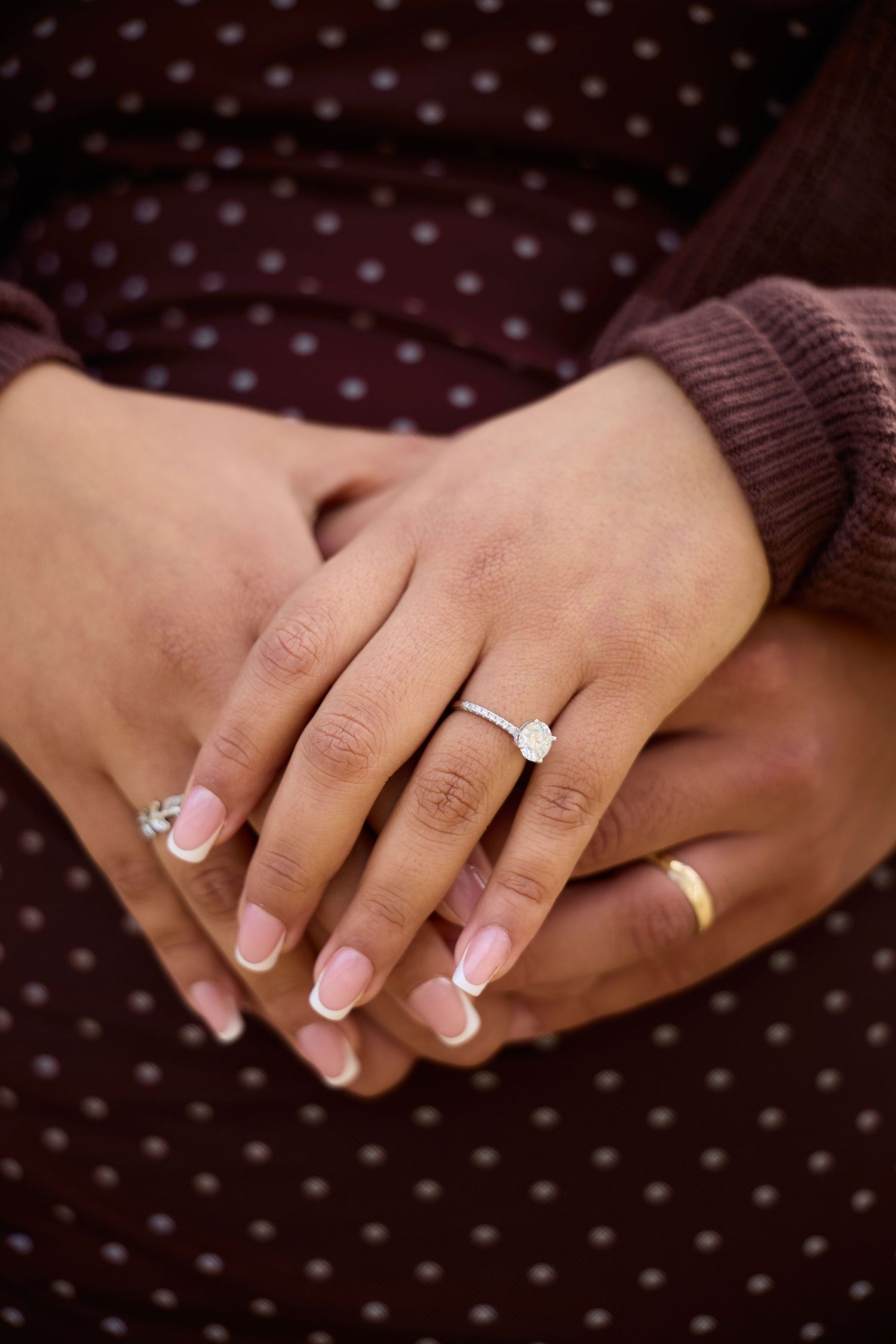 Close-up shots of hands wearing a diamond engagement ring and wedding band against a dark polka dot background.
