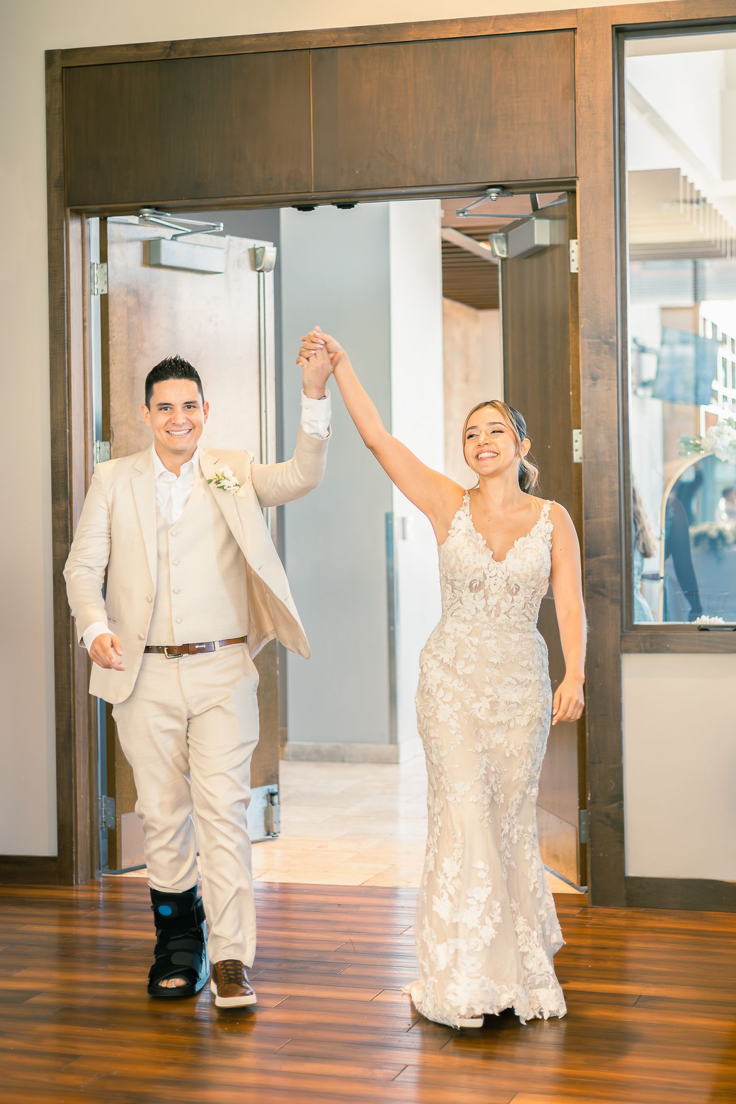 Wedding couple dances joyfully across a polished wooden floor in a bright indoor venue.