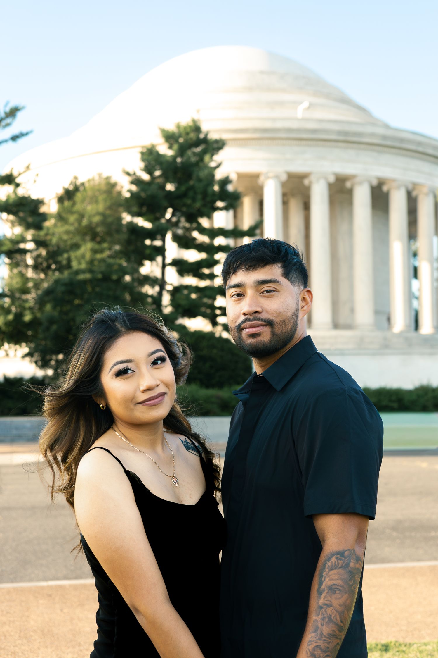 A couple in black outfits poses together in front of the Jefferson Memorial during a sunset photoshoot.