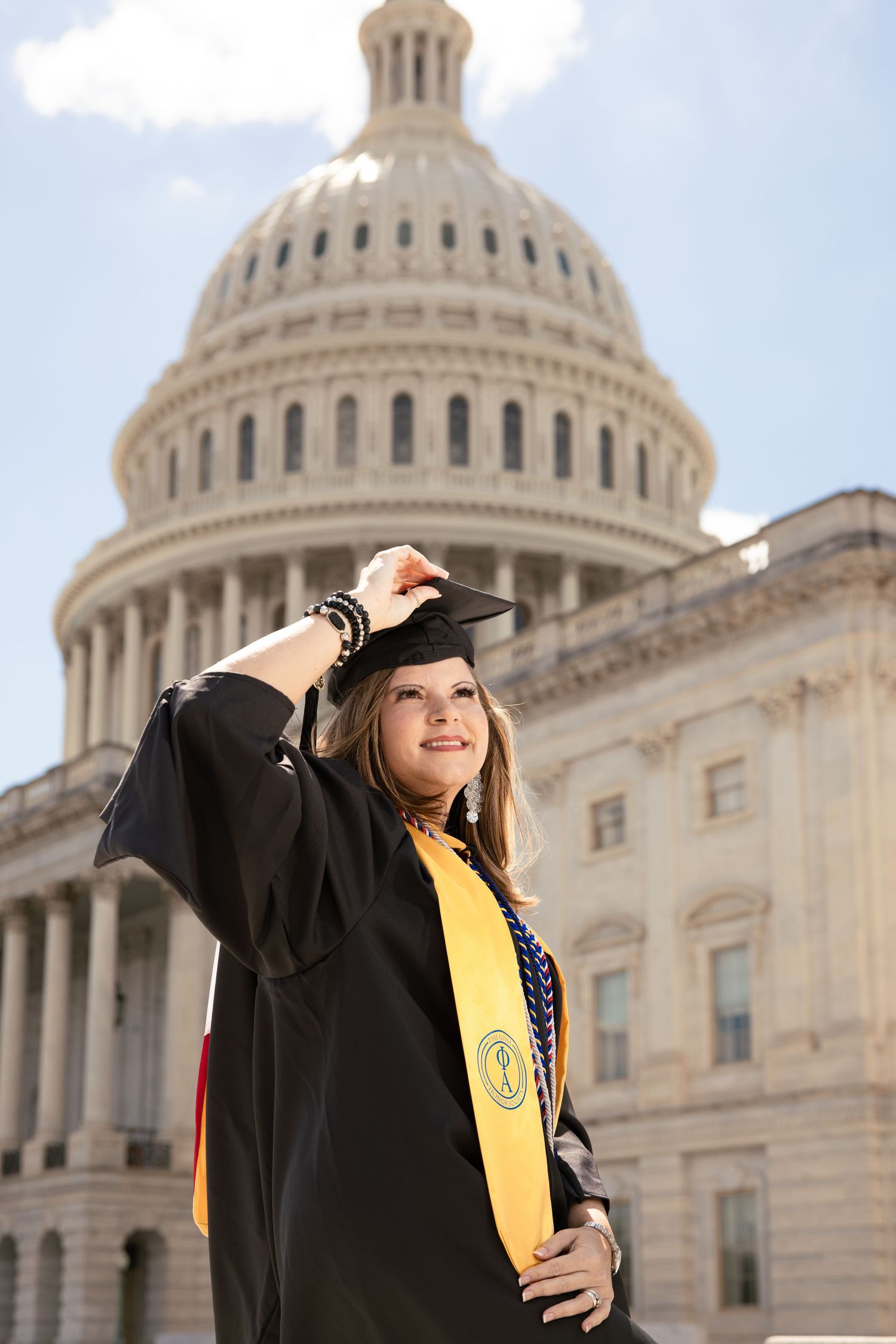 A graduate in cap and gown poses in front of the United States Capitol Building dome on graduation day.