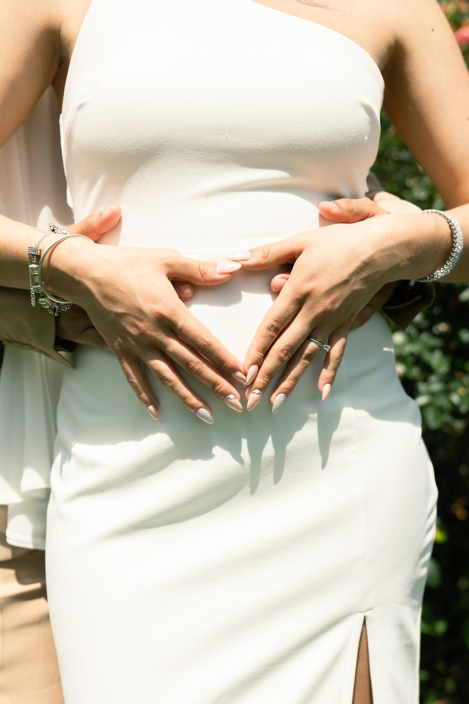 Row of bridesmaids in elegant white dresses showing off rings against a natural outdoor background.