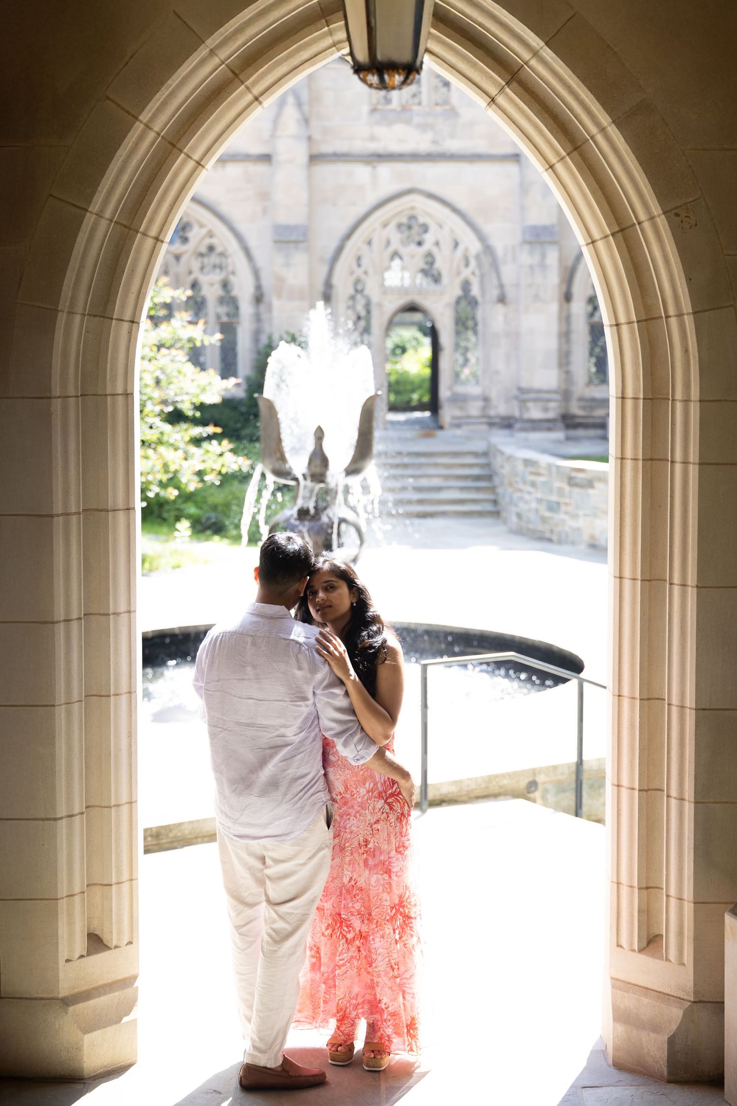 A couple embraces under a Gothic stone archway with white balloons, surrounded by elegant architectural details.